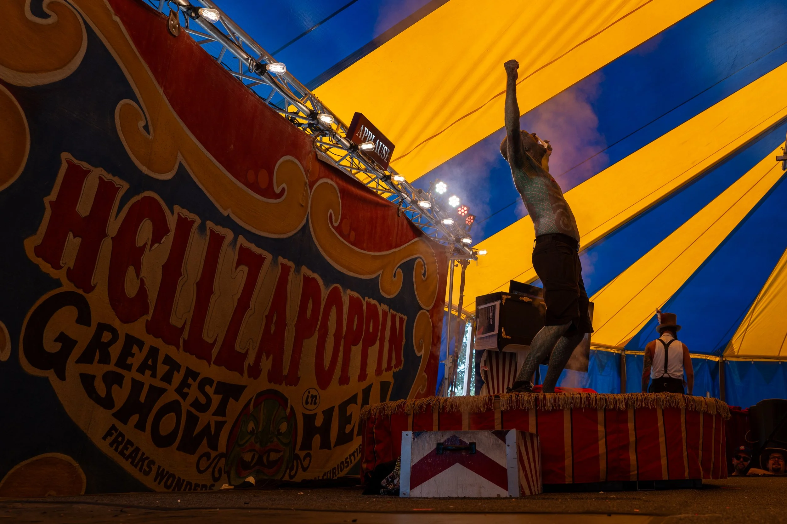 Circus tent interior with a performer on a platform and another person in costume near the back.