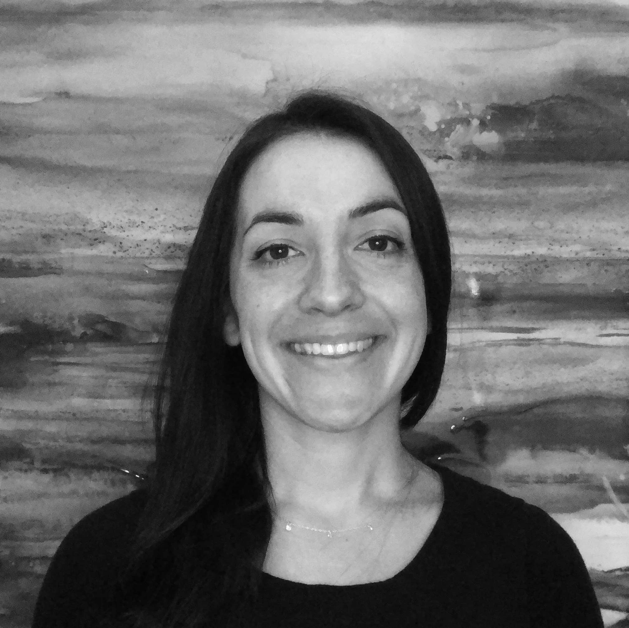 A woman with long dark hair smiling in front of an abstract watercolor painting.