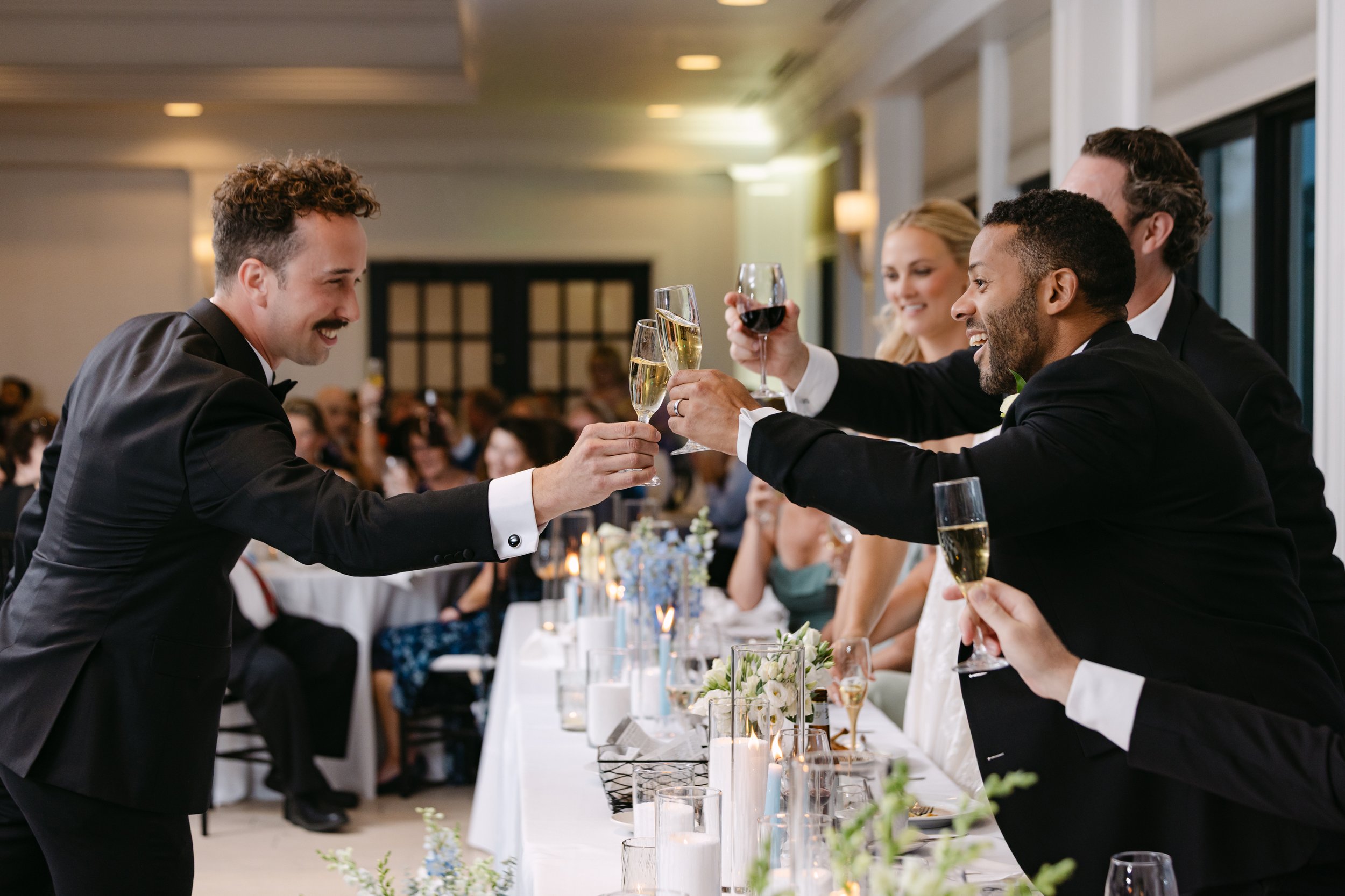 People in formal attire celebrating with glasses of champagne and wine at a wedding reception.
