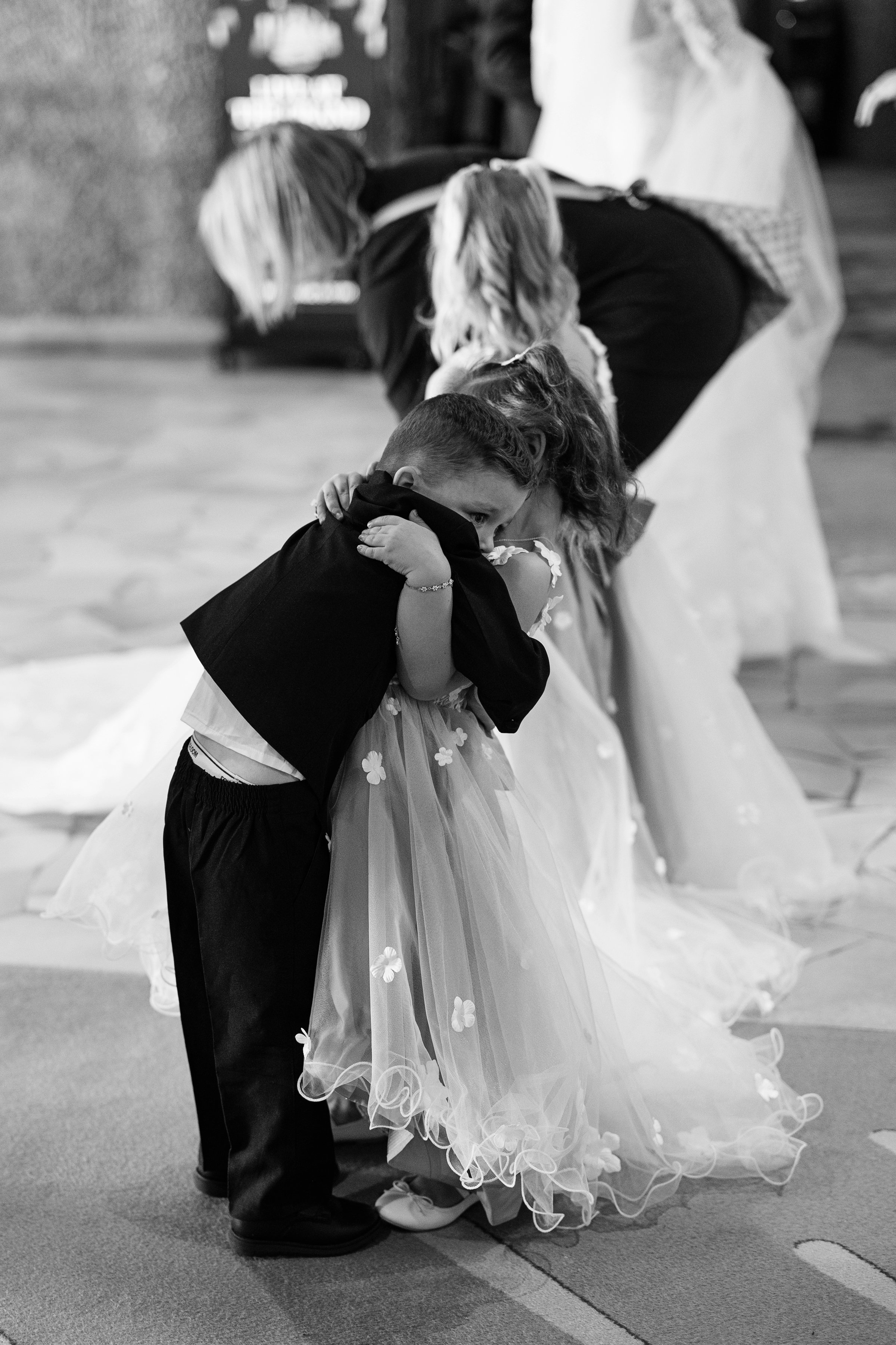A young girl in a floral dress hugging a boy in a suit at a wedding ceremony.