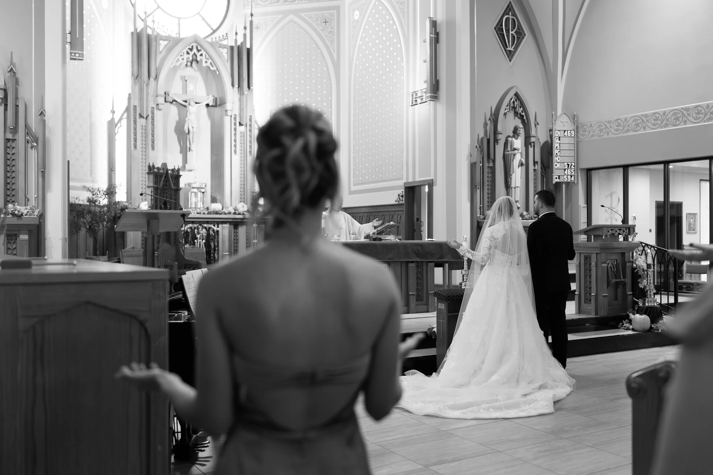 A bride and groom standing at the altar during a wedding ceremony in a church, with a guest in the foreground watching them.