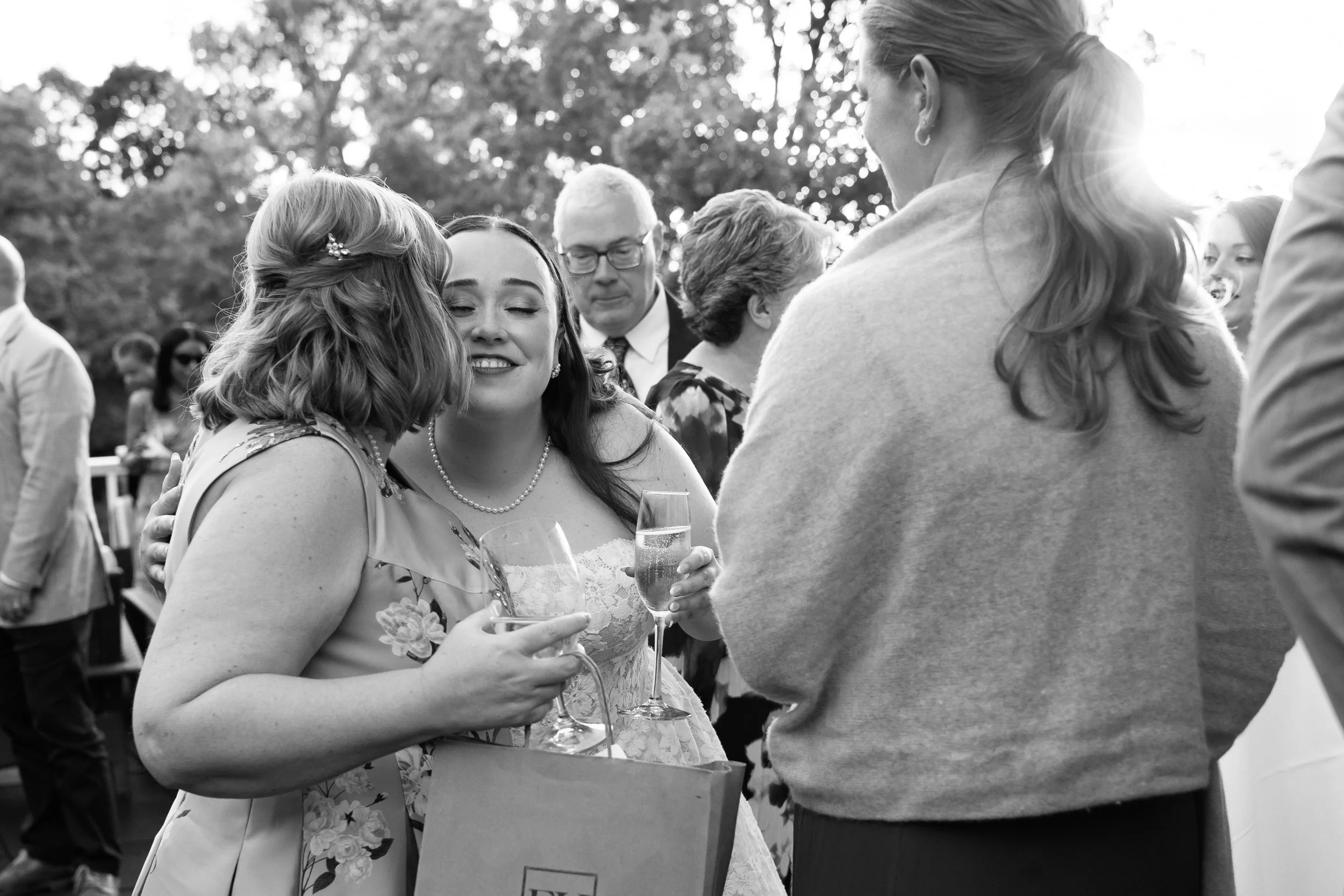 People at a social gathering, celebrating with drinks, outdoors with trees in the background, black and white photograph.