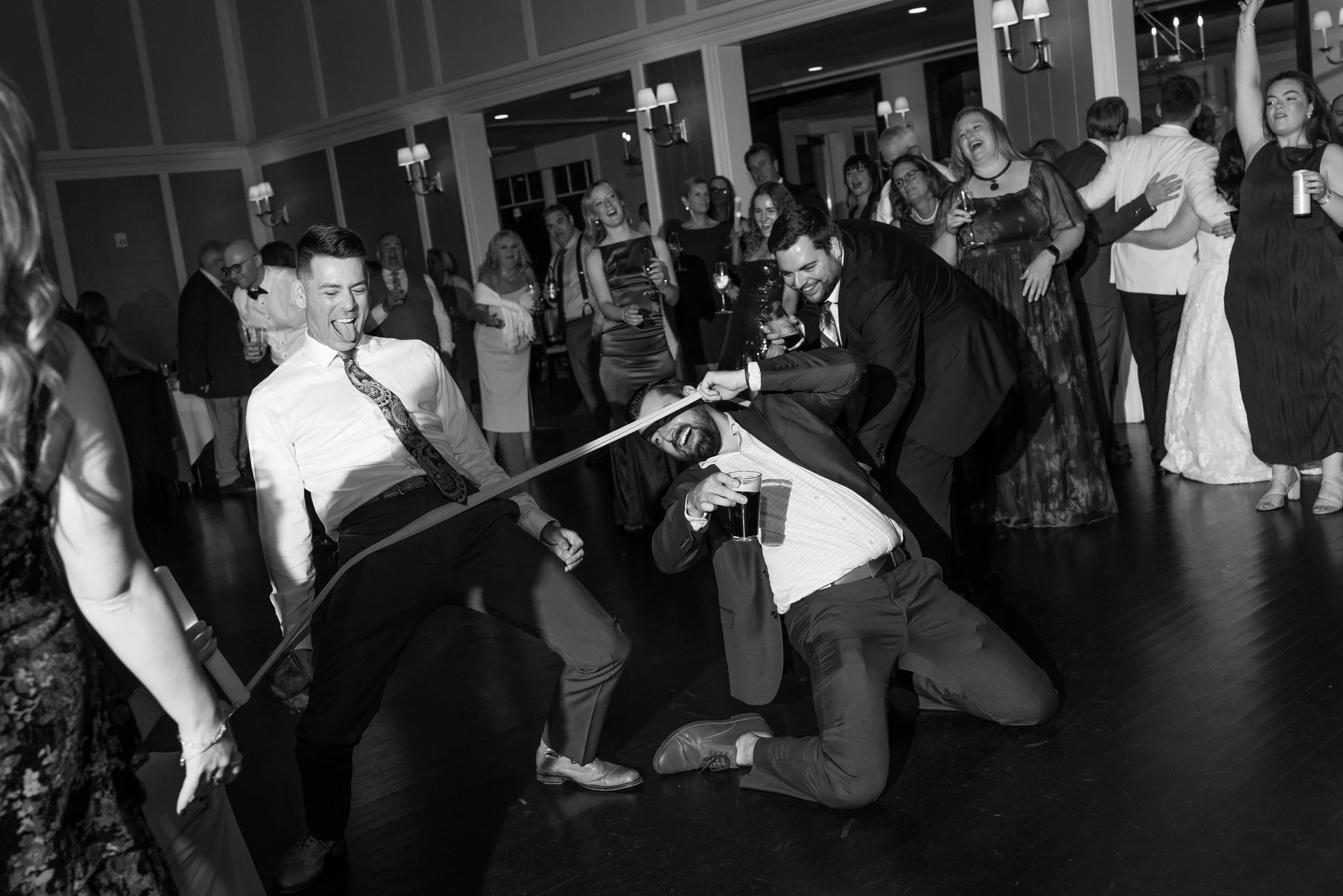 People dancing and having fun at a party, with some engaged in a playful tug-of-war over a beer.