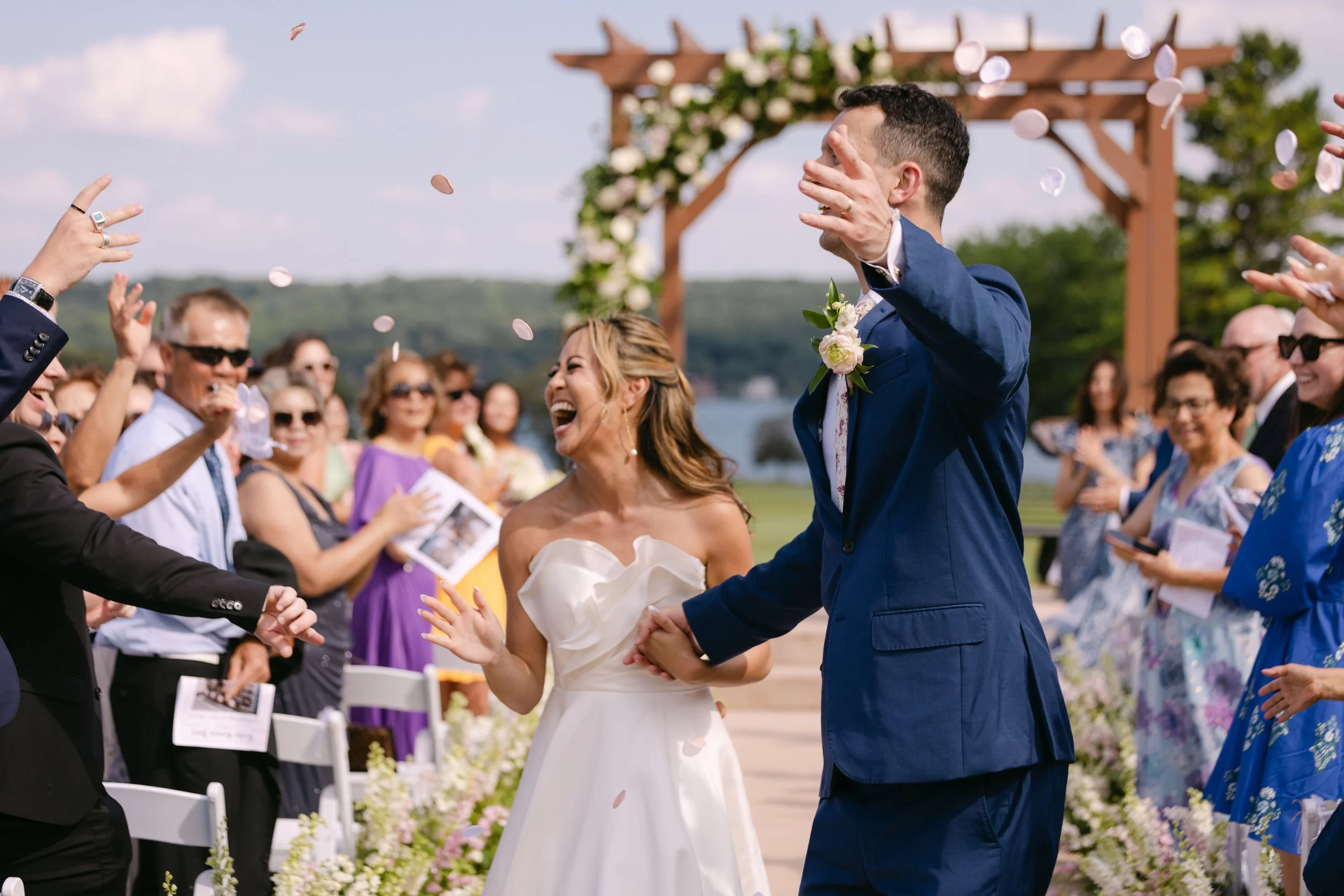 A bride and groom are celebrating at their outdoor wedding ceremony, surrounded by friends and family, with confetti falling around them.