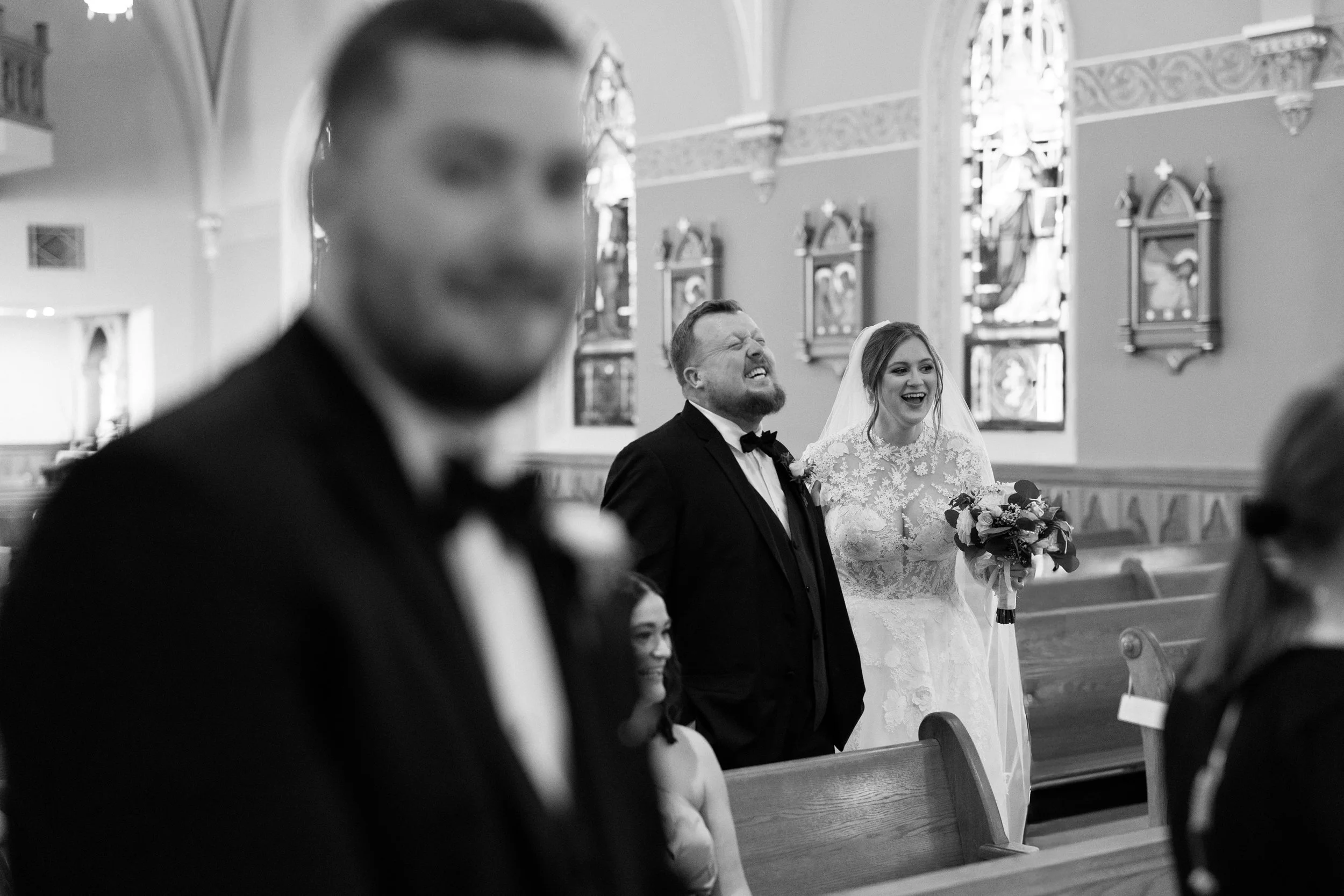 Bride and groom at a wedding ceremony inside a church, smiling and holding hands, with guests seated in pews.