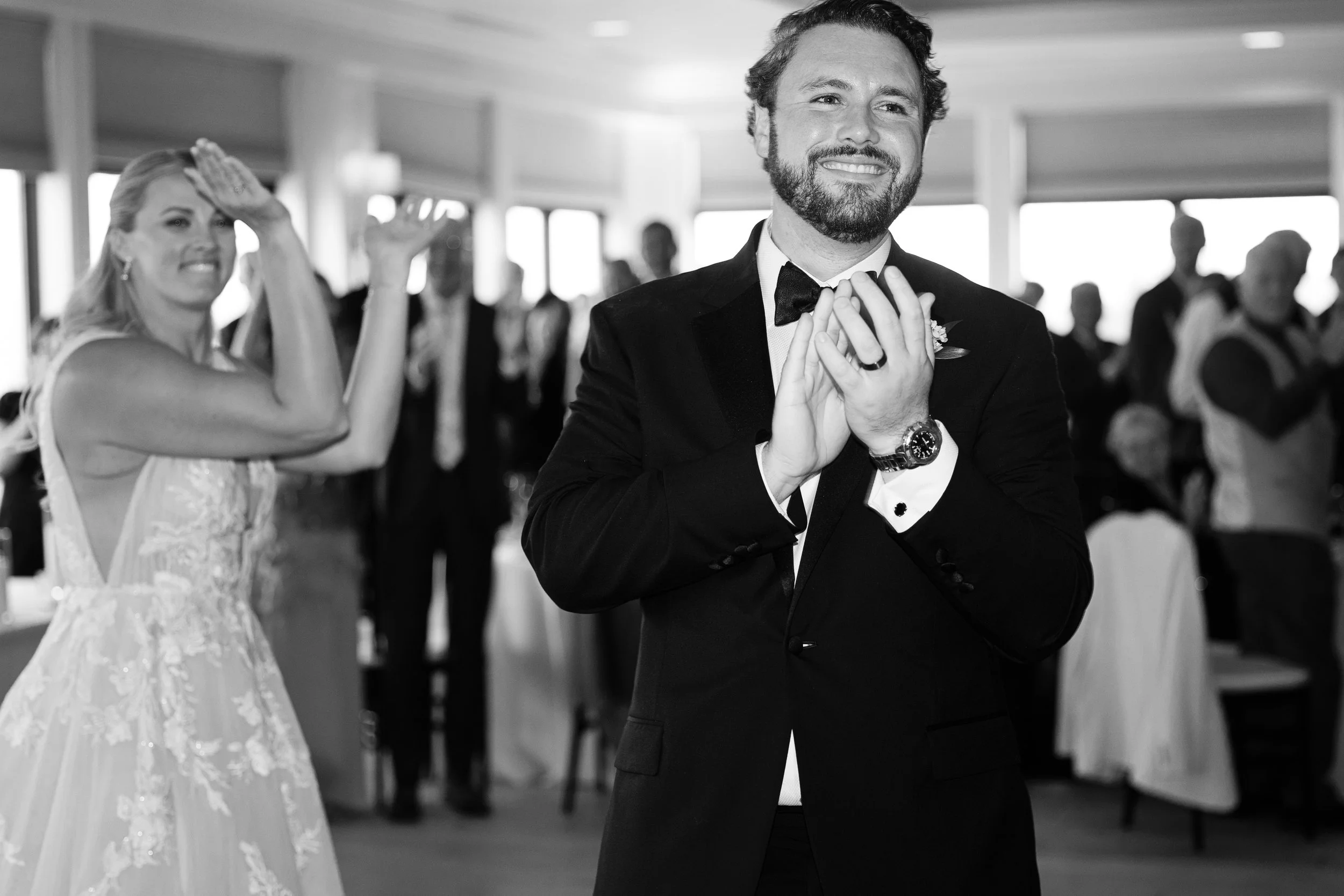 A groom in a tuxedo and a bride in a wedding dress celebrating at their wedding reception.