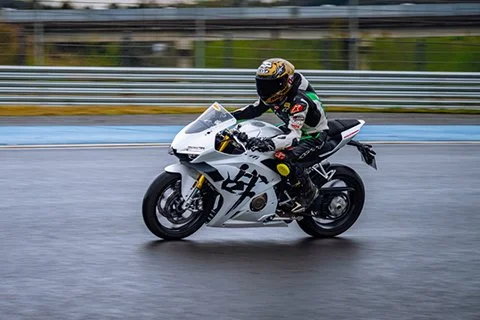 Motorcycle rider on a wet road wearing a helmet and racing gear.