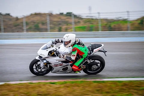 Motorcyclist in racing gear riding on a white sport motorcycle on a wet track.
