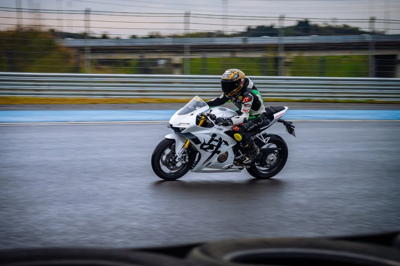 A motorcyclist wearing a helmet and racing suit riding a white sportbike on a wet race track.