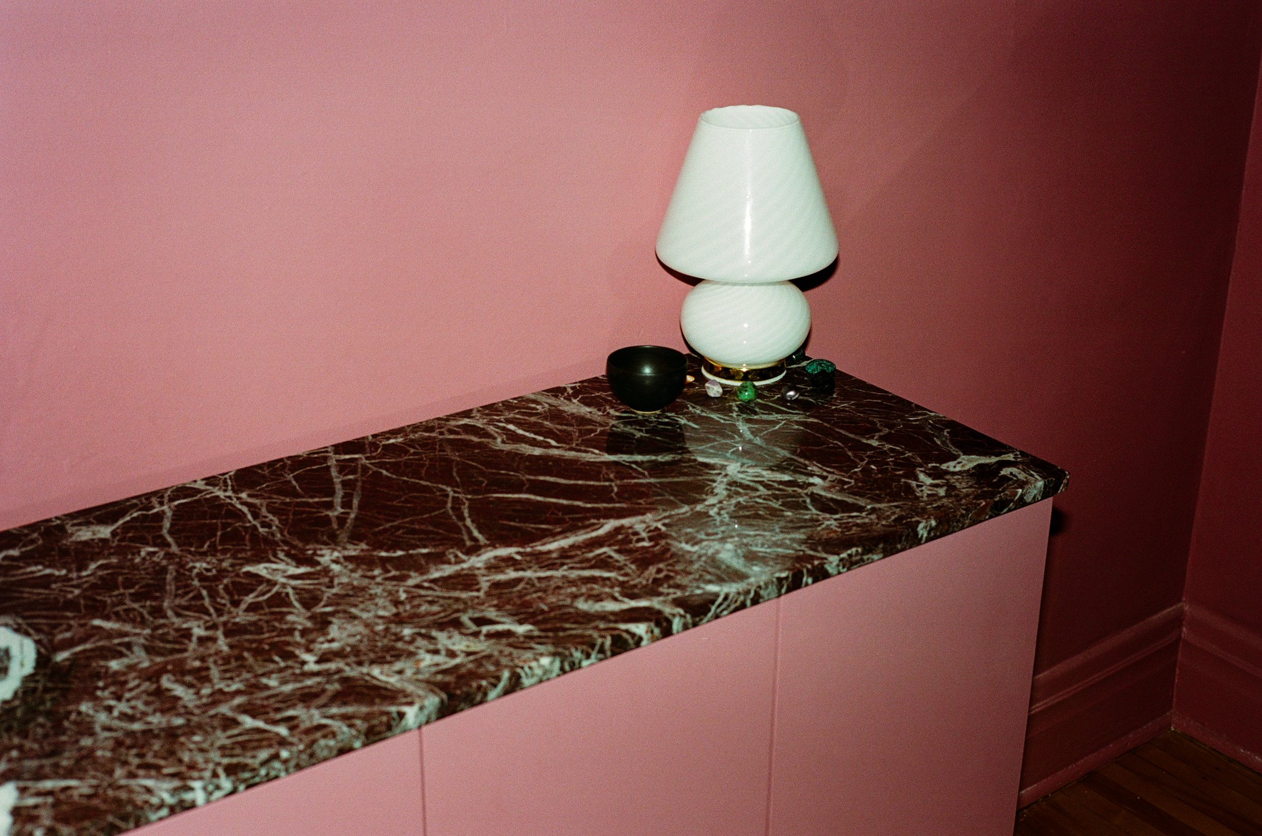 Détail comptoir en marbre vert foncé avec lampe blanche, mur rose