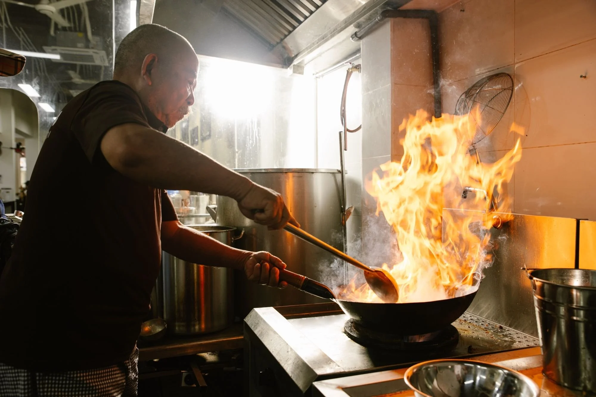 A chef cooking with a large flame in a professional kitchen.