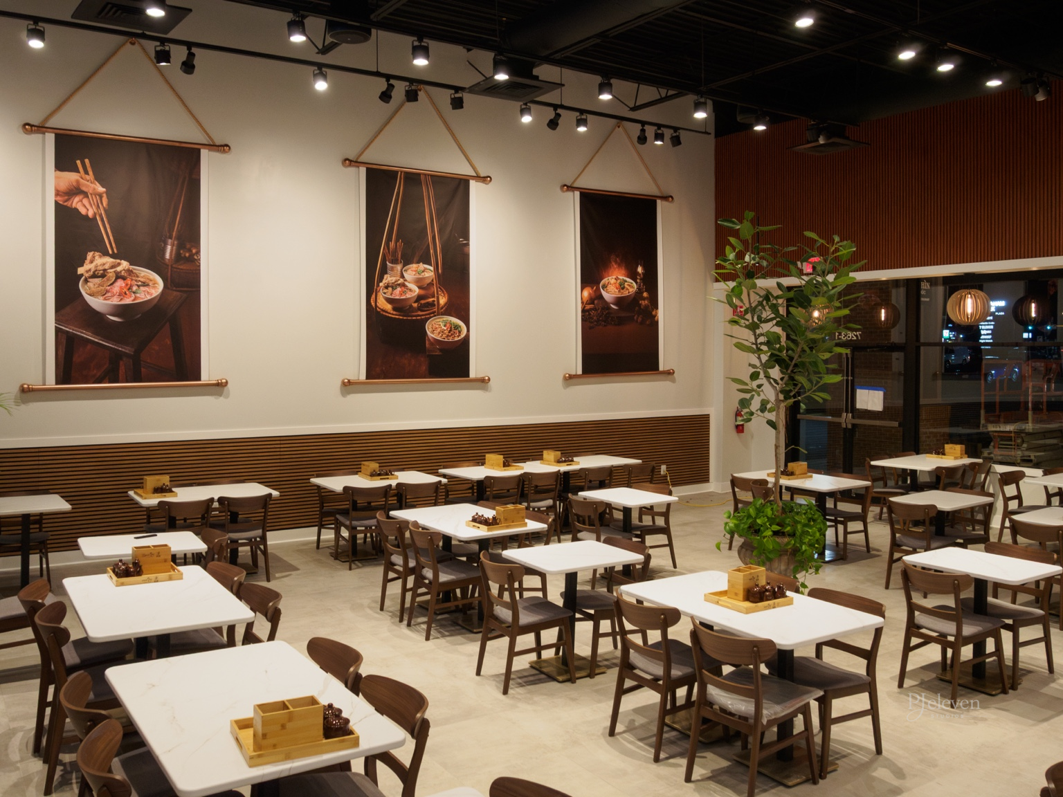 Empty modern Asian restaurant with white tables, wooden chairs, and large food-themed wall art.