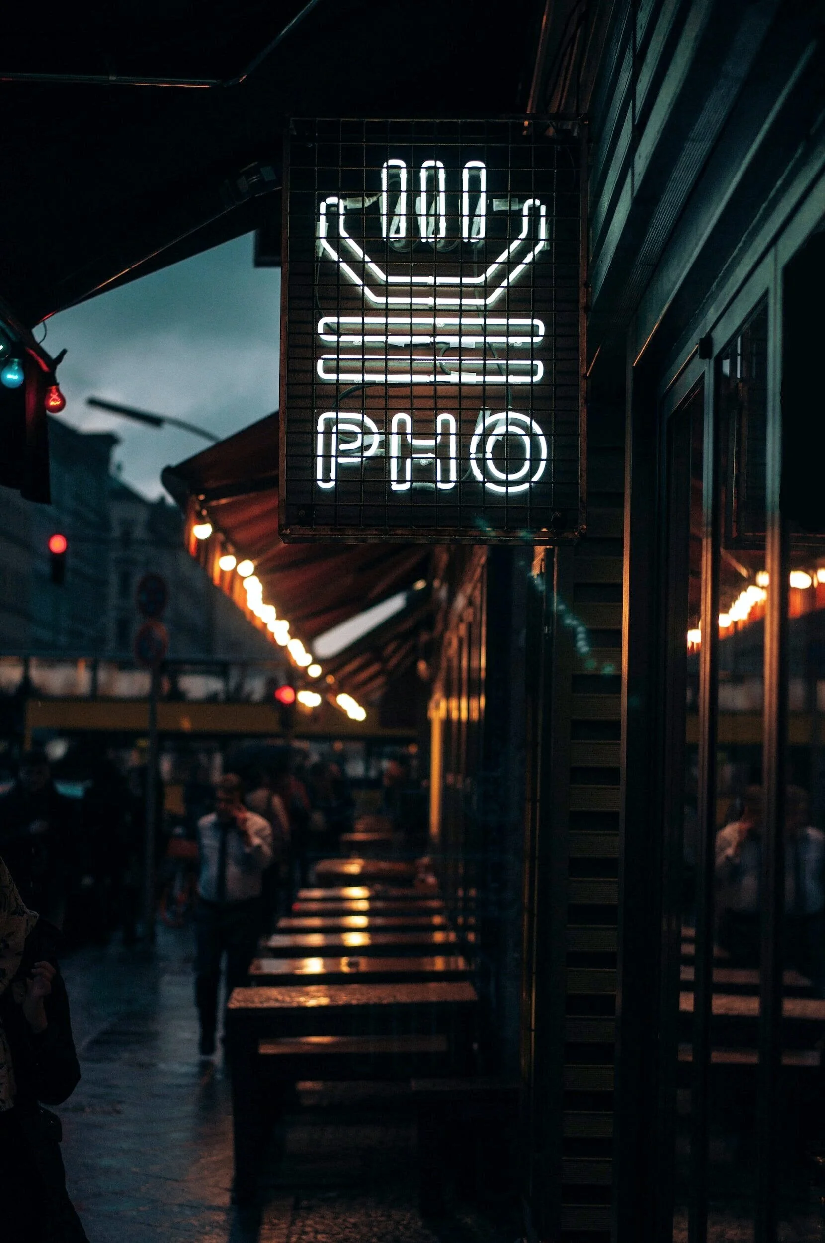 Neon sign with a burger and the word 'PHO' at an outdoor street food market in the evening.