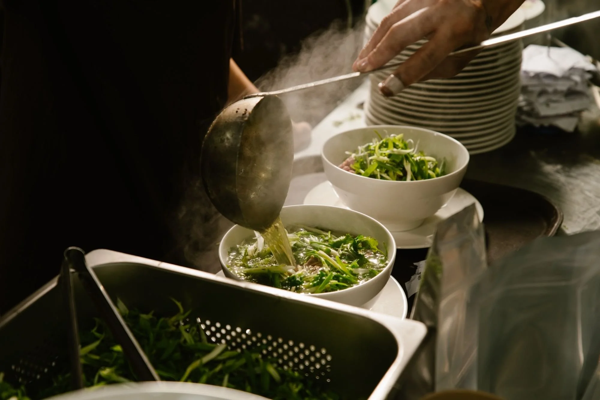 A person serving soup over green onion into bowls with fresh green onion in the background.