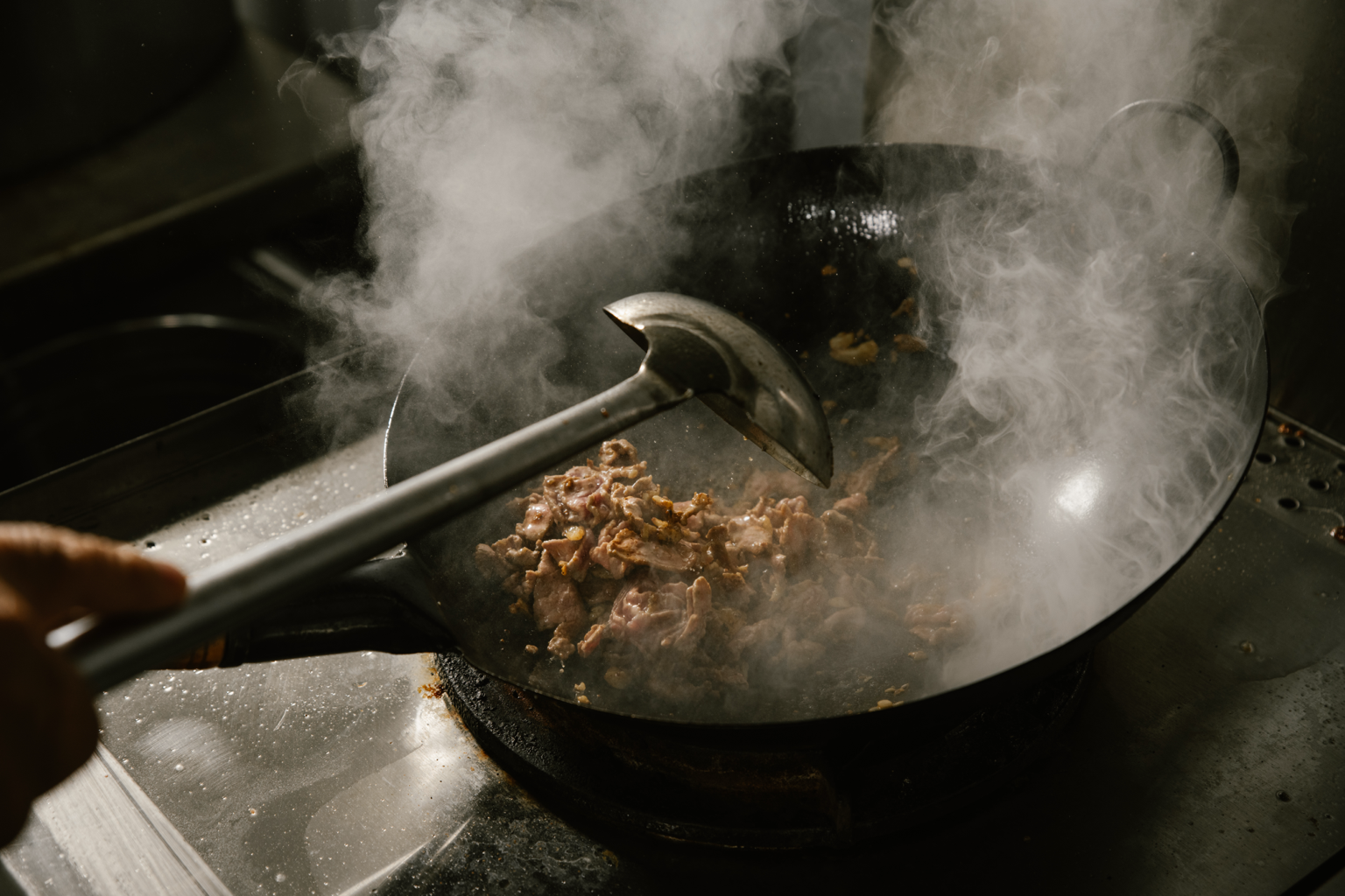 Stir-frying ribeye beef in a wok on a stovetop with steam rising.