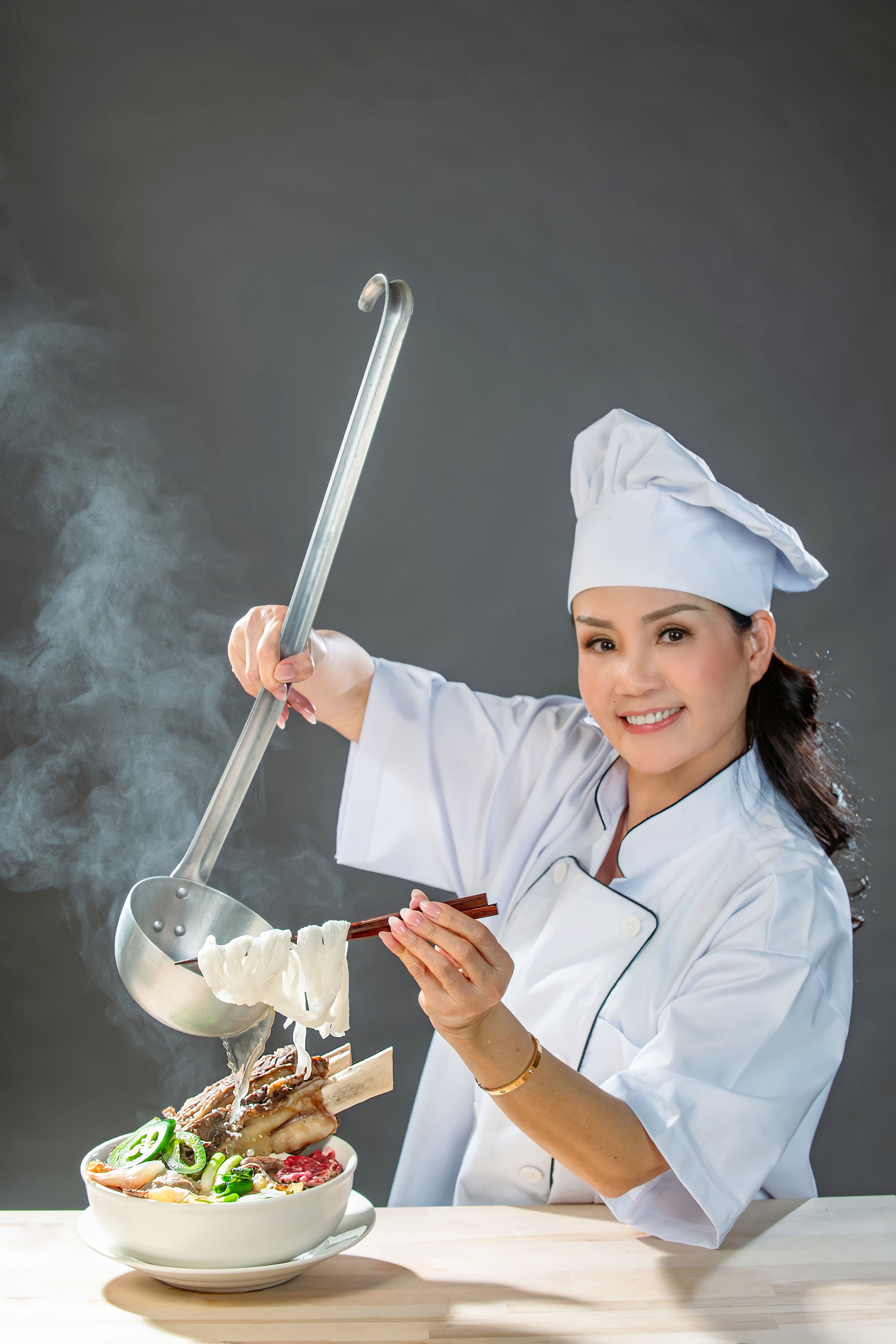 A woman dressed as a chef serving hot pho beef noodles soup with beef ribs with chopsticks, with steam rising from the bowl.