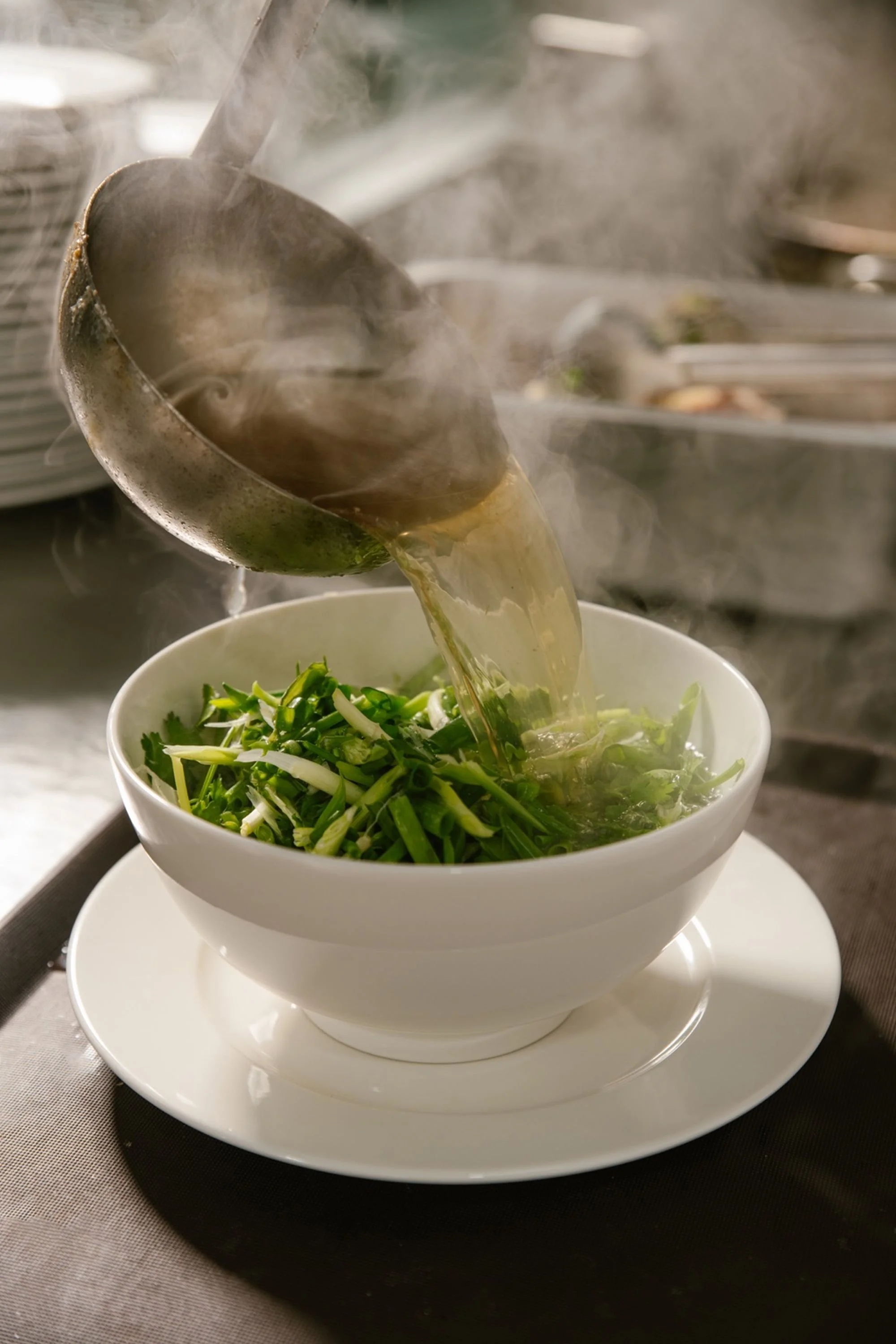 Hot broth being poured over fresh green onions in a white bowl.