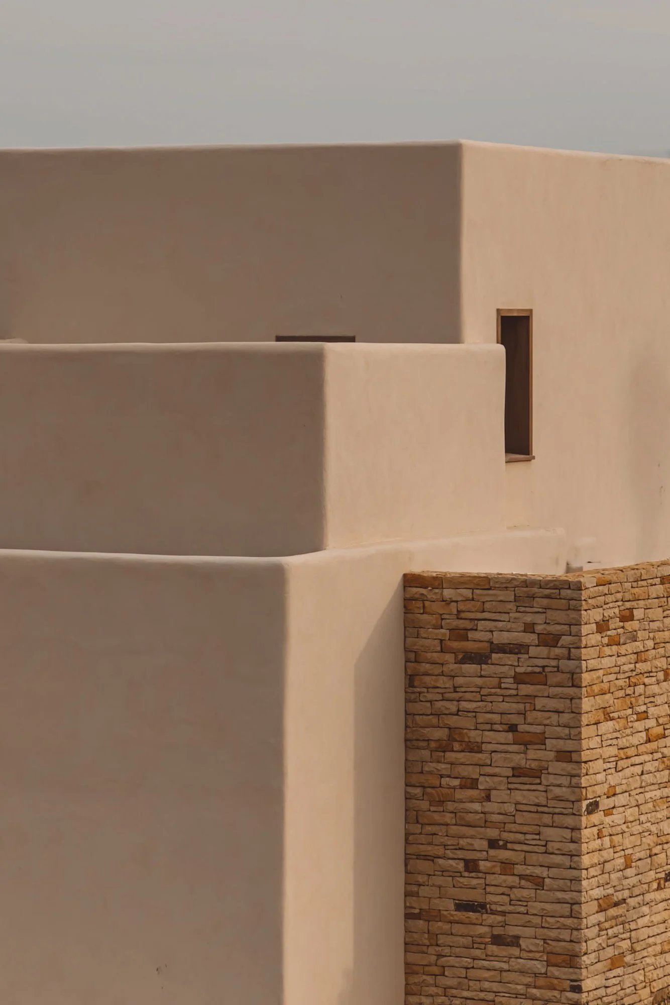 Close-up of a modern building with smooth beige curved walls and a brown brick corner detail. Royal Mansour Tamuda Bay Morocco. Photography Sophia van den Hoek