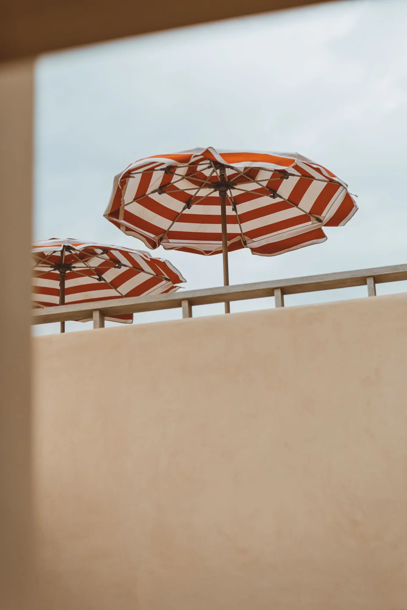 View of red and white striped beach umbrellas seen from below, against a cloudy sky. Royal Mansour Tamuda Bay Morocco. Photography Sophia van den Hoek