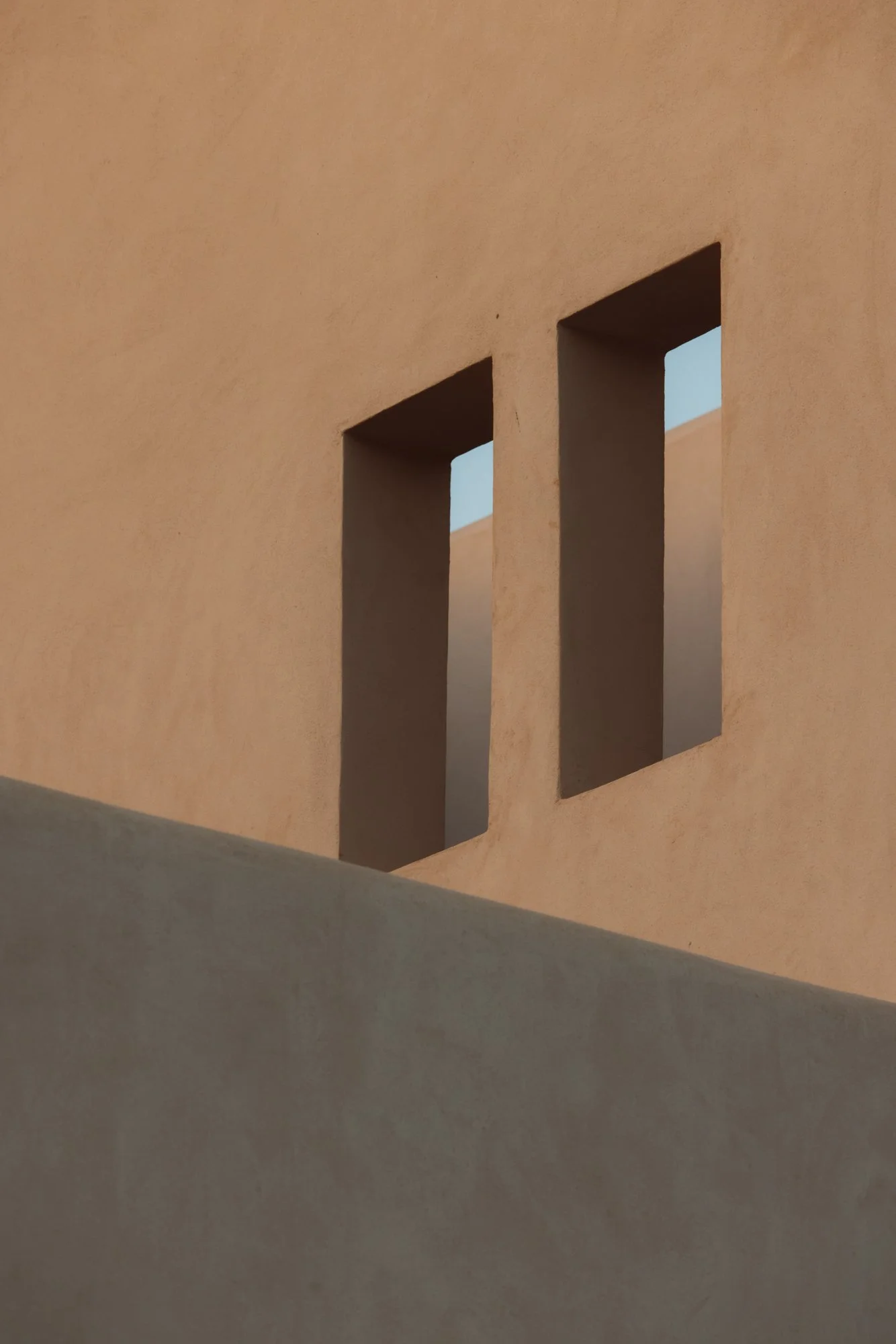 Close-up of a beige wall with two rectangular windows showing the sky. Royal Mansour Tamuda Bay Morocco. Photography Sophia van den Hoek