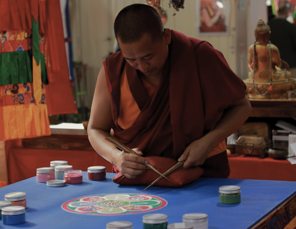 Moine bouddhiste en habit traditionnel éxécutant un mandala coloré dans un temple devant la statue de bouddha