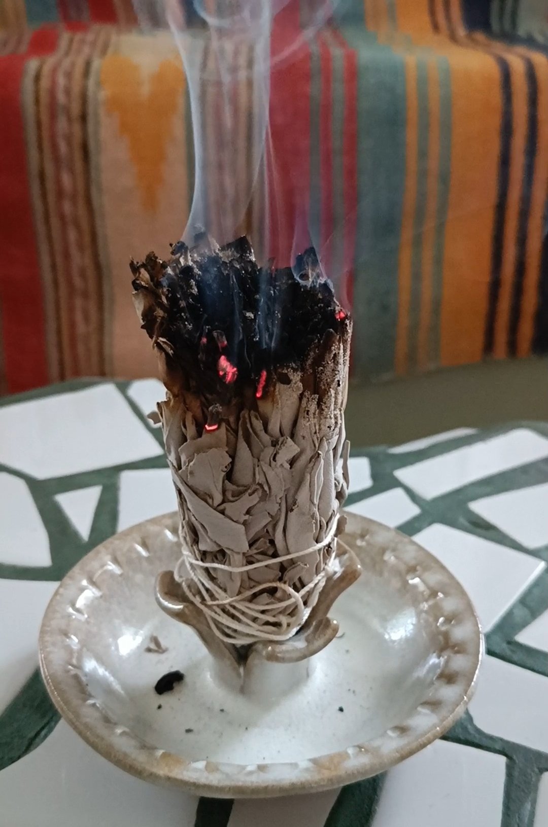 Un bâton de sauge qui fume dans un porte bougie en grès émaillé de la collection Chélidoine blanche