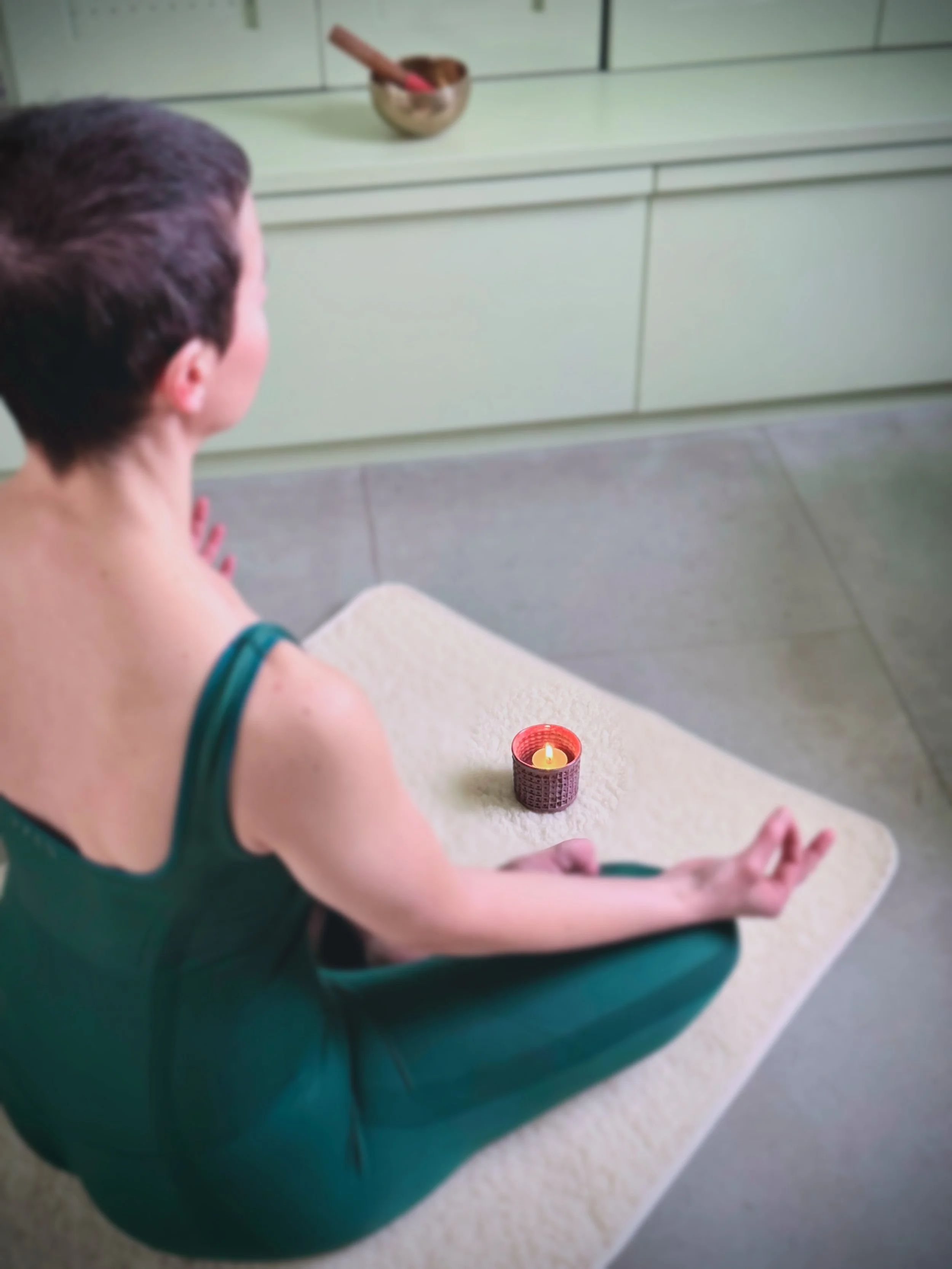 Une personne en position de méditation assise en tailleur sur un tapis, avec une bougie allumée devant elle, dans une pièce calme et épurée.