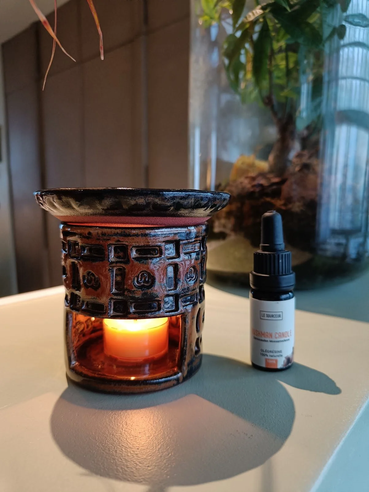 Bougie allumé dans un diffuseur d'huiles essentielles en grès de la collection Oeil de tigre et son flacon d'huile essentielle posé à côté