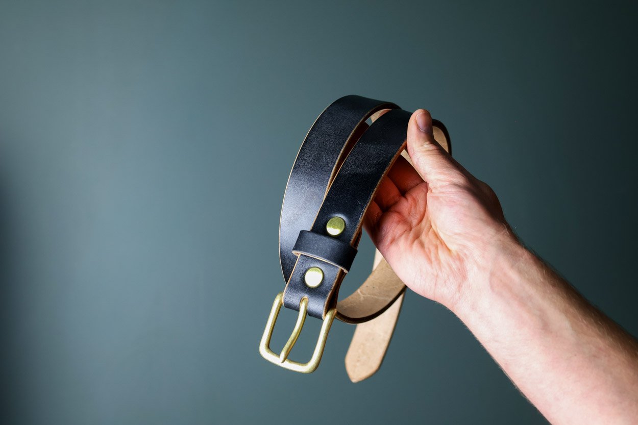 UK made black leather men's belt with gold buckle being held in hand