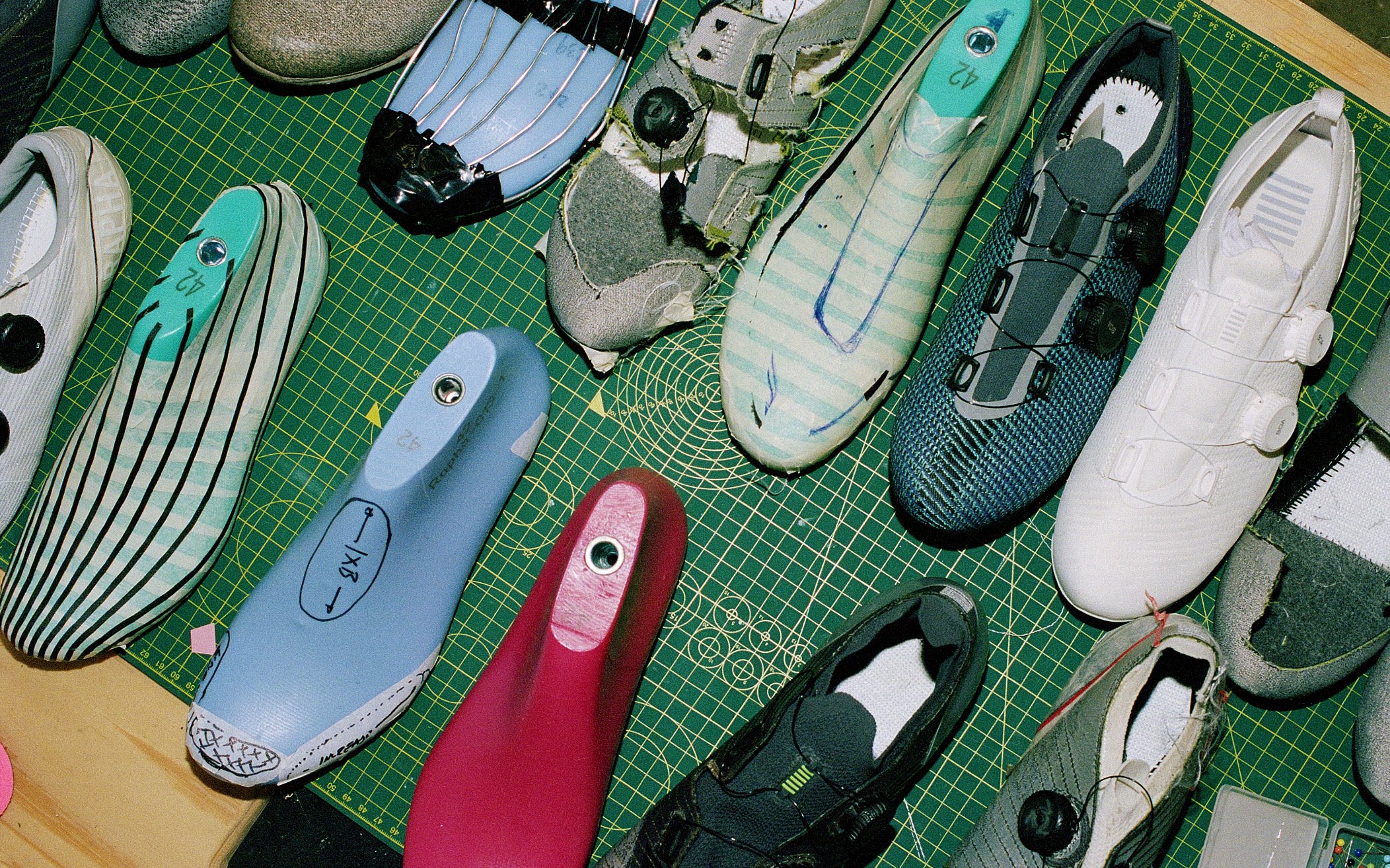 Several pairs of athletic shoes and insoles arranged on a green cutting mat, with some shoes tagged or labeled.