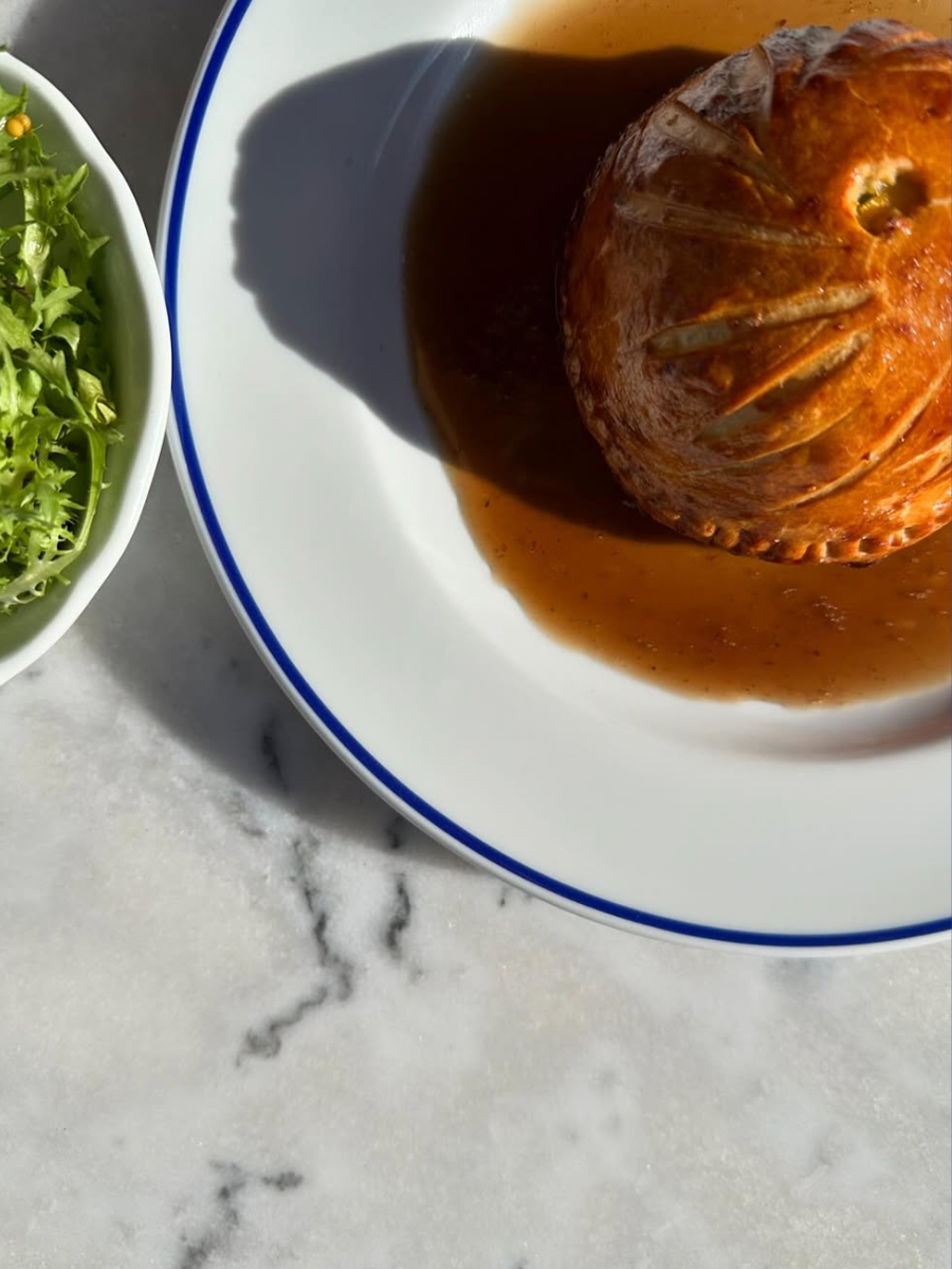 Baked stuffed tomato on a white plate with a blue rim, next to a bowl of green salad on a gray marble surface.