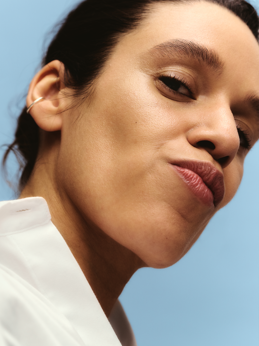 Close-up of a woman with dark hair, wearing minimal makeup, slightly smiling against a light blue background.