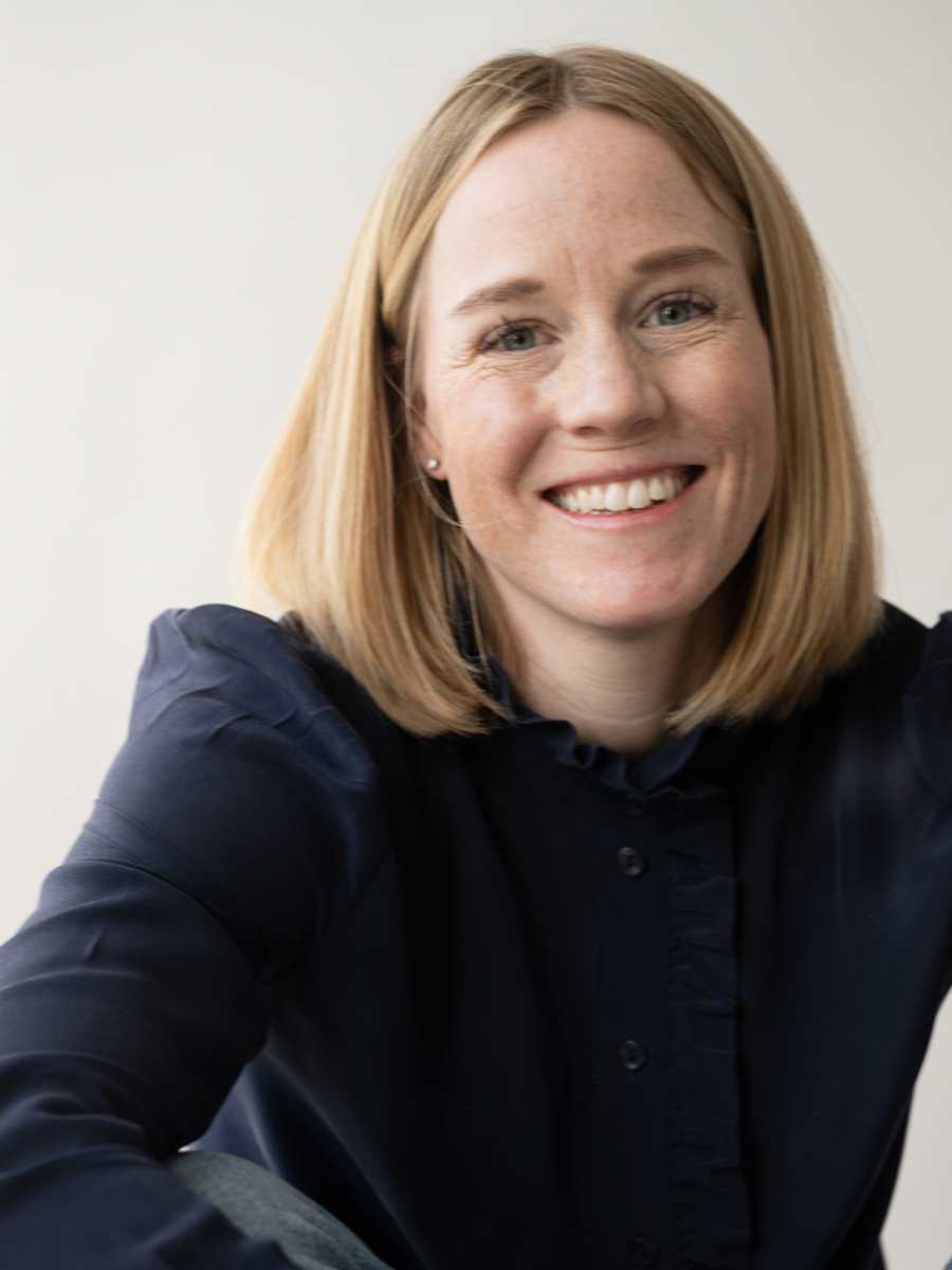 A smiling woman with shoulder-length blonde hair, wearing a dark shirt, looking at the camera.