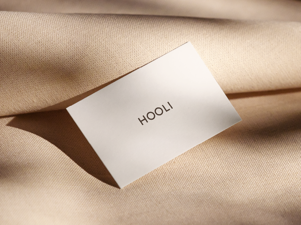 A white clothing tag with the brand name 'HOOLI' attached to beige fabric.