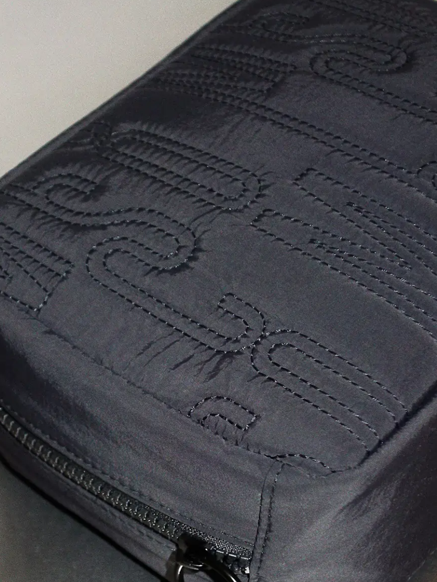 Close-up of a black fabric bag with stitched text that appears to spell 'Versace'.