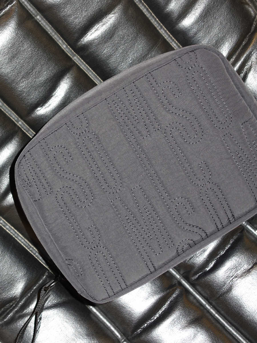 A rectangular gray fabric pouch with stitched text that appears to read 'FASHION' in a repeated pattern, placed on a shiny black leather surface.