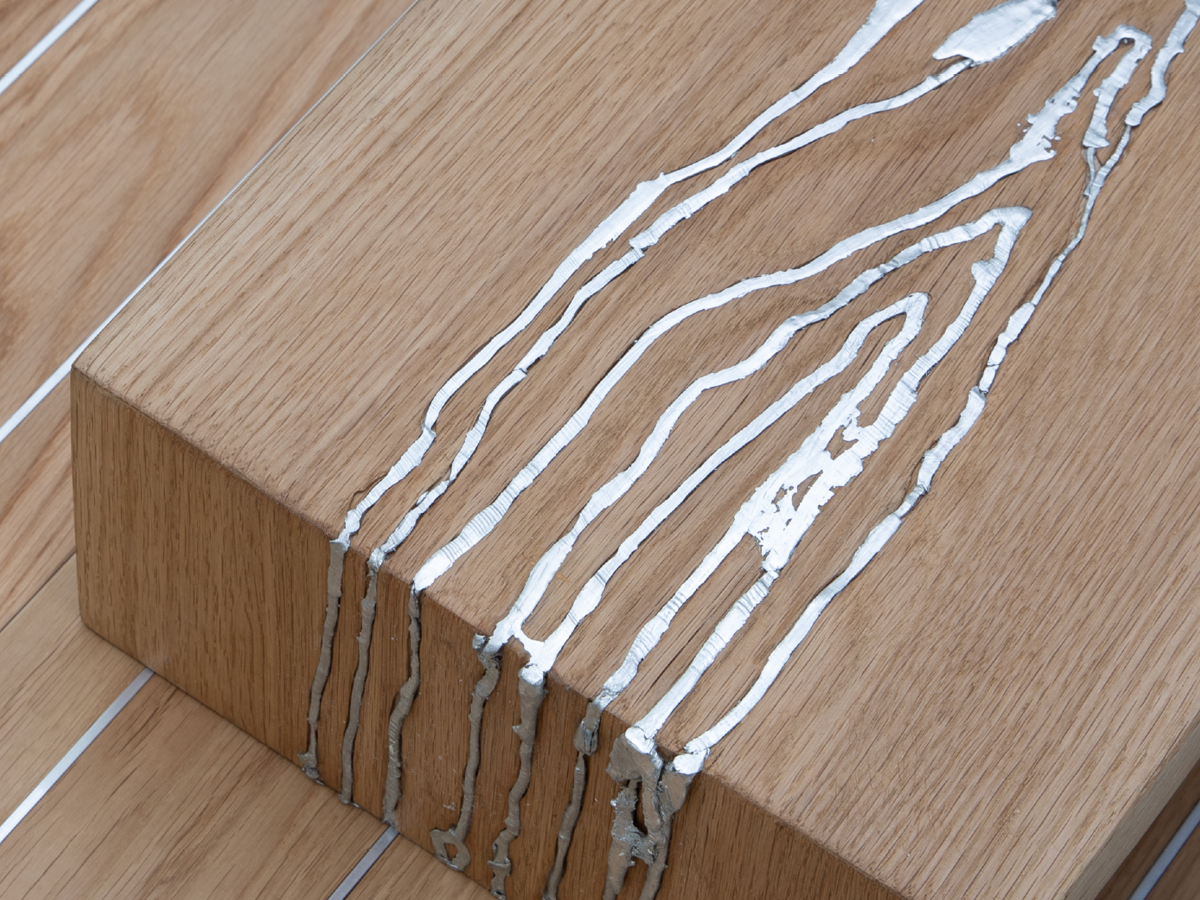 A close-up of a wooden table with visible cracks, revealing white and gray materials inside.