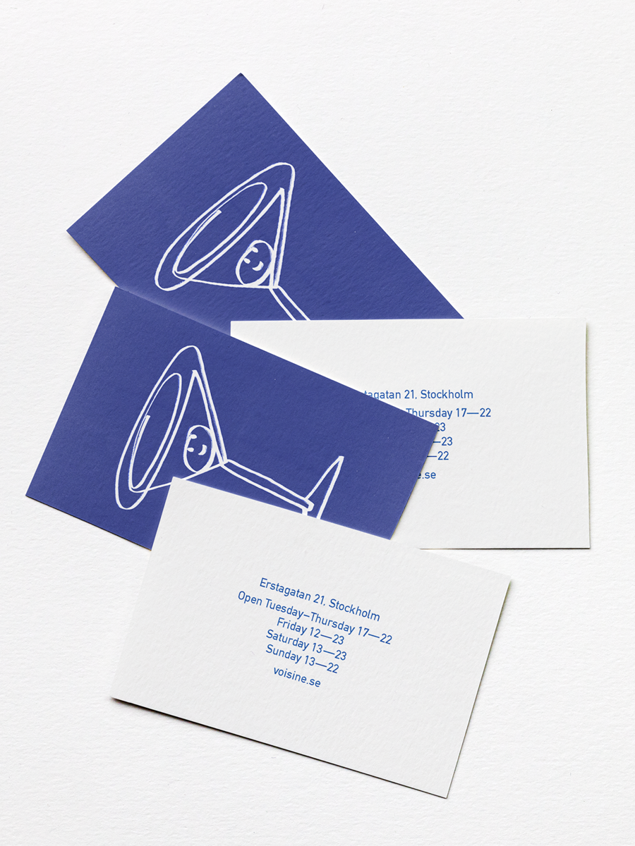 Two business cards and one white card with blue text. One business card is dark blue with a white line drawing of a martini glass. The other dark blue card has the same illustration, and the white card contains address and opening hours for Voisine i