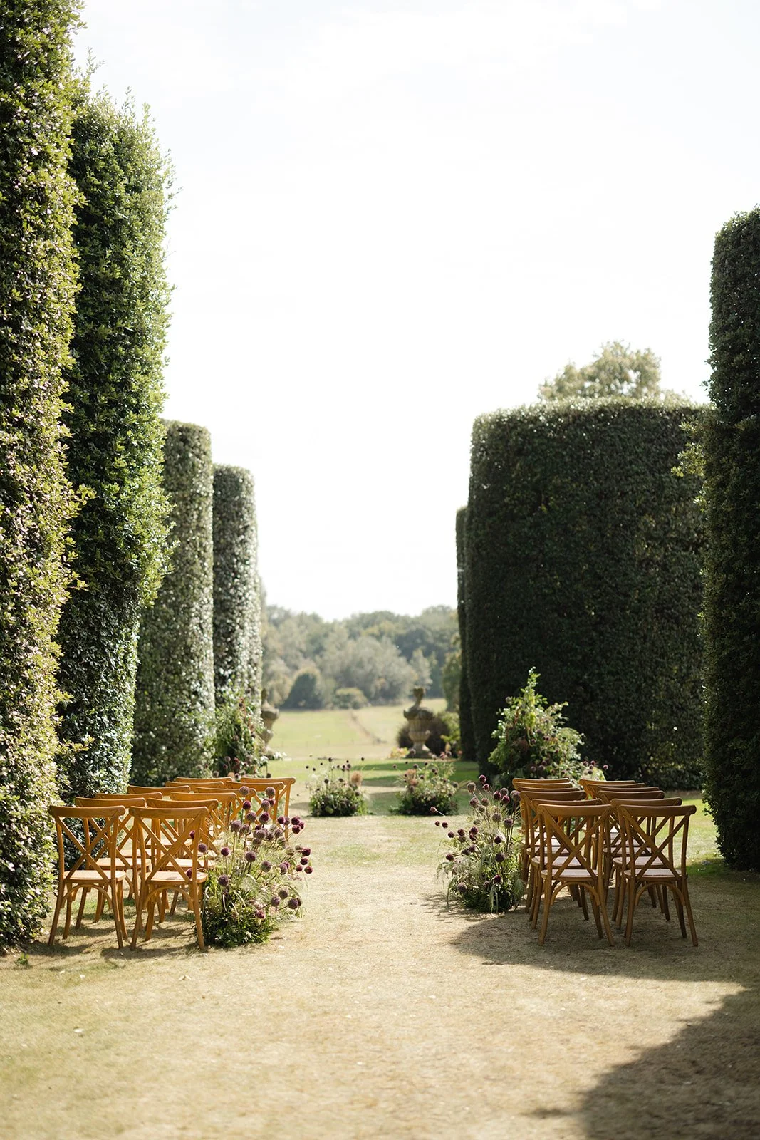 A couple dressed in formal wedding attire, with the man wearing a dark brown tuxedo and the woman in a white wedding gown, holding a bouquet of white and beige flowers against a dark background.