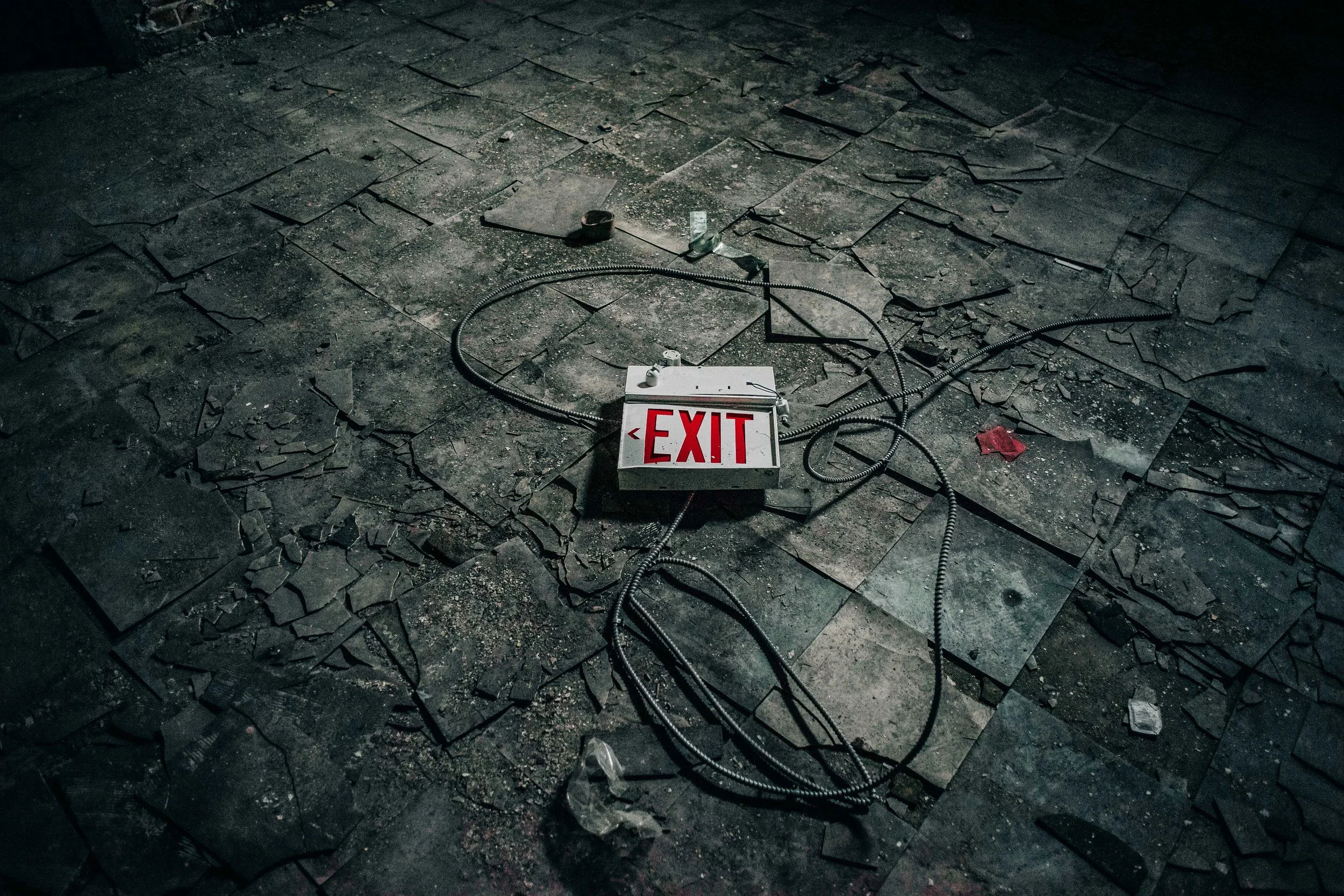 PIcture of a Red and White exit sign lying on the stone ground surrounded by cords from the sign