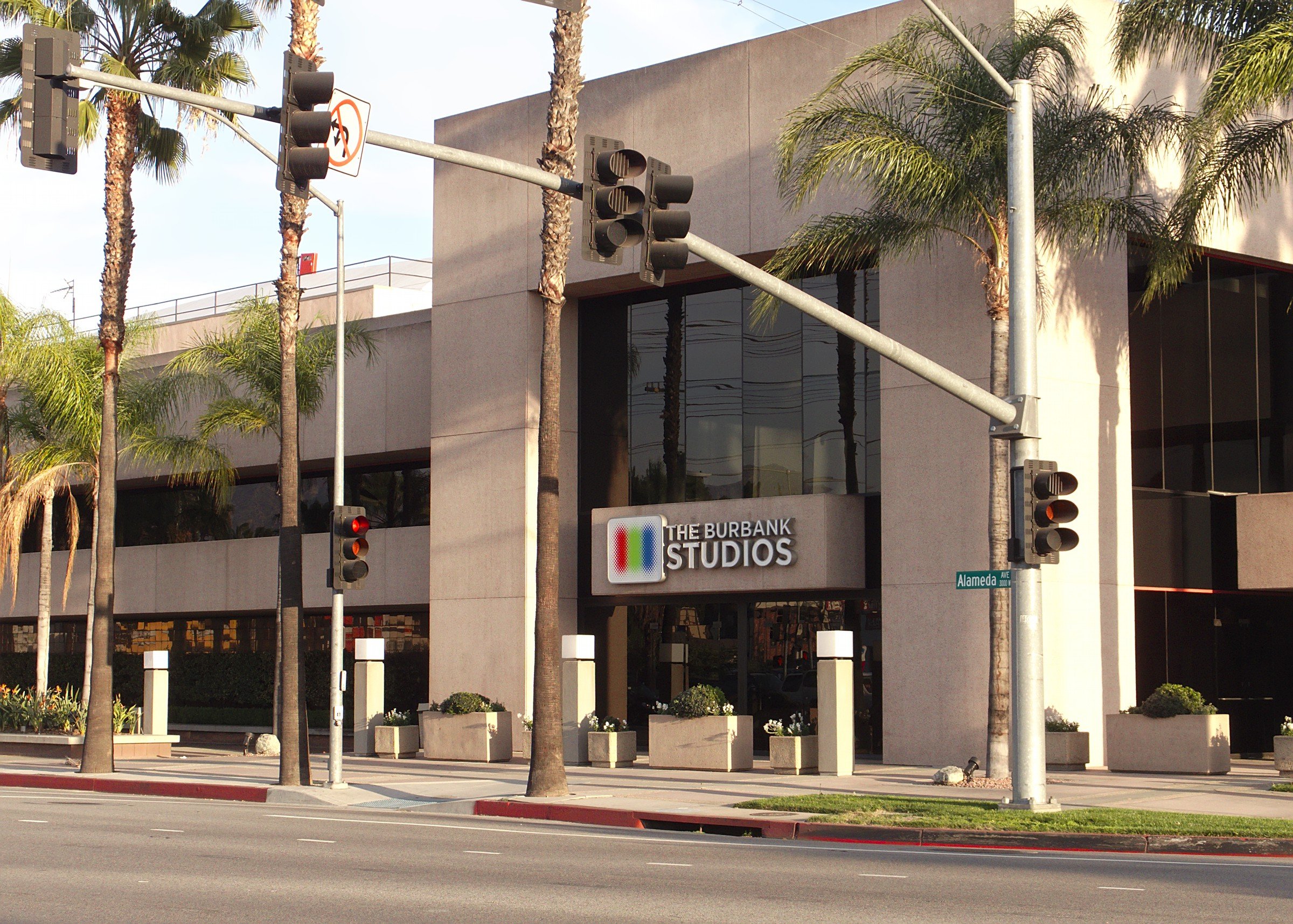 Exterior view of The Burbank Studios building with palm trees, street traffic lights, and a sign on the building, located at the corner of Alameda Avenue.