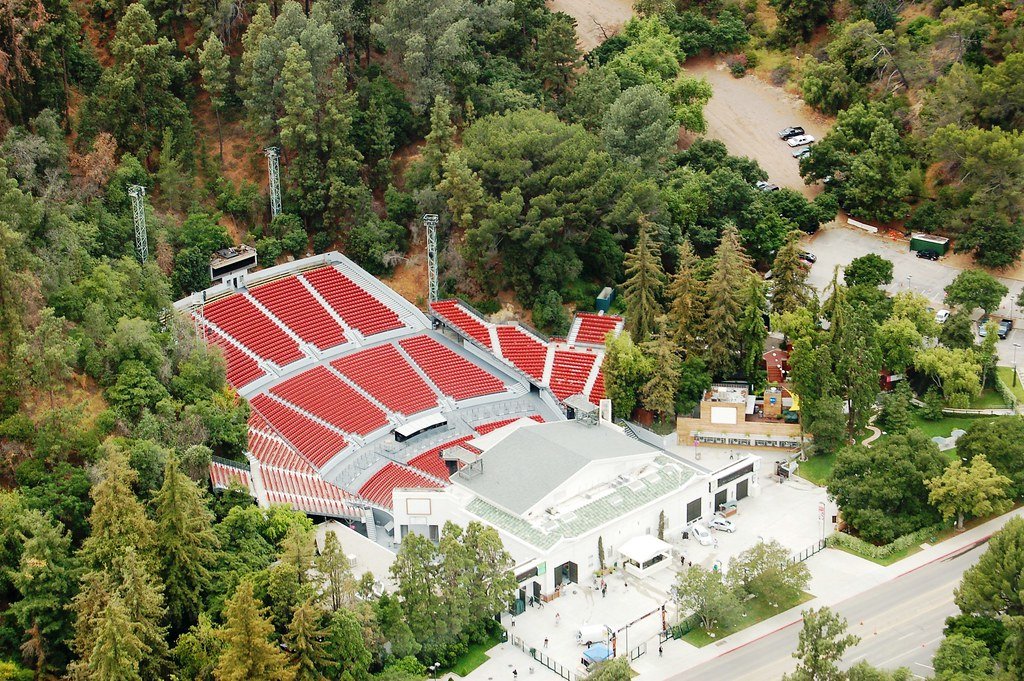 A large outdoor amphitheater with red seats surrounded by trees in a natural setting.