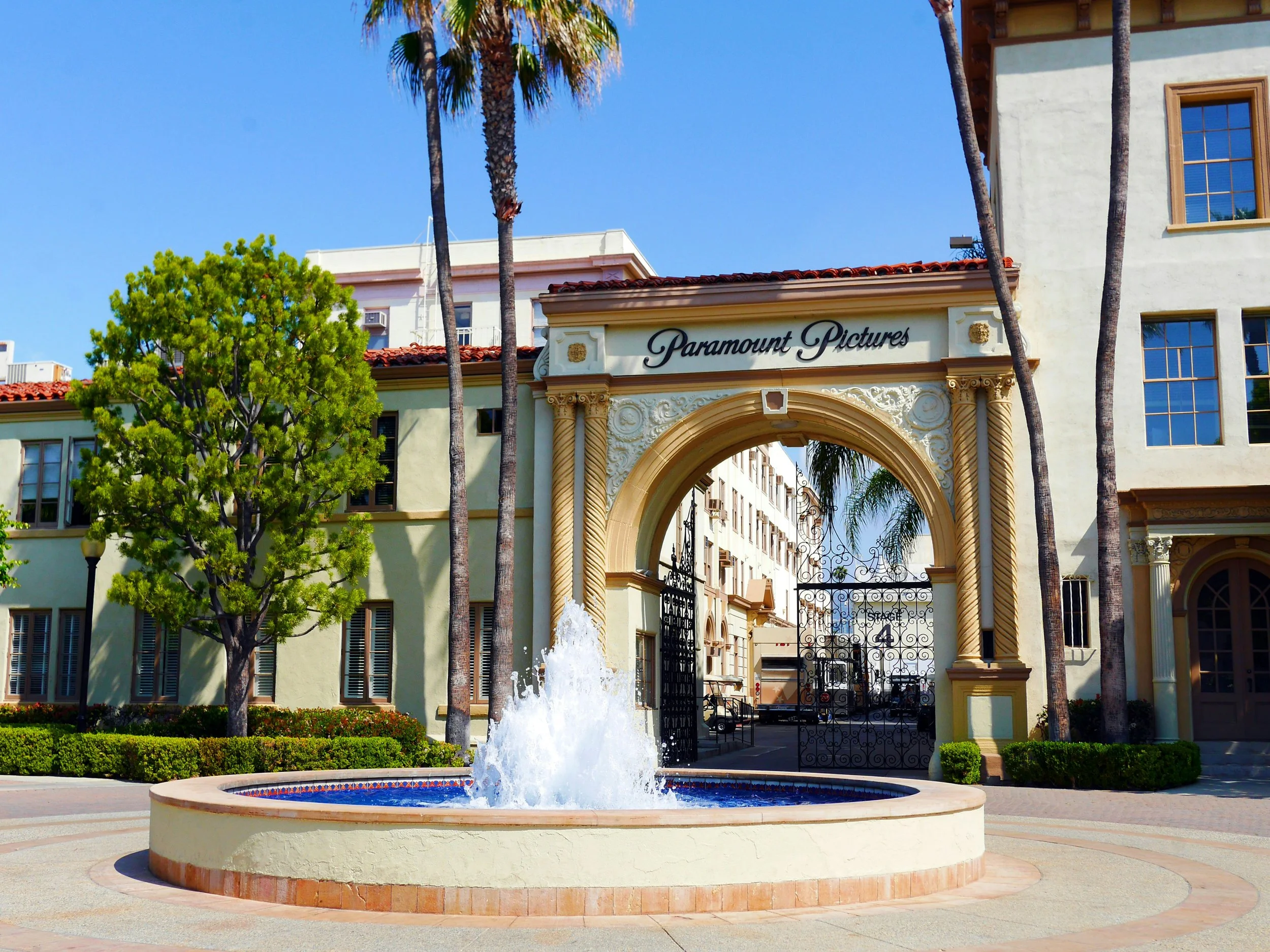 Entrance gate to Paramount Pictures with fountain in the foreground, palm trees, and a clear blue sky.