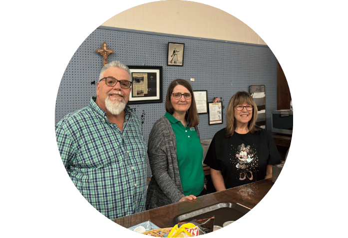 Three people standing behind a counter in an office or reception area, smiling at the camera.