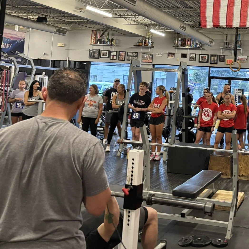 A man spots a competitor bench pressing while other competitors watch.