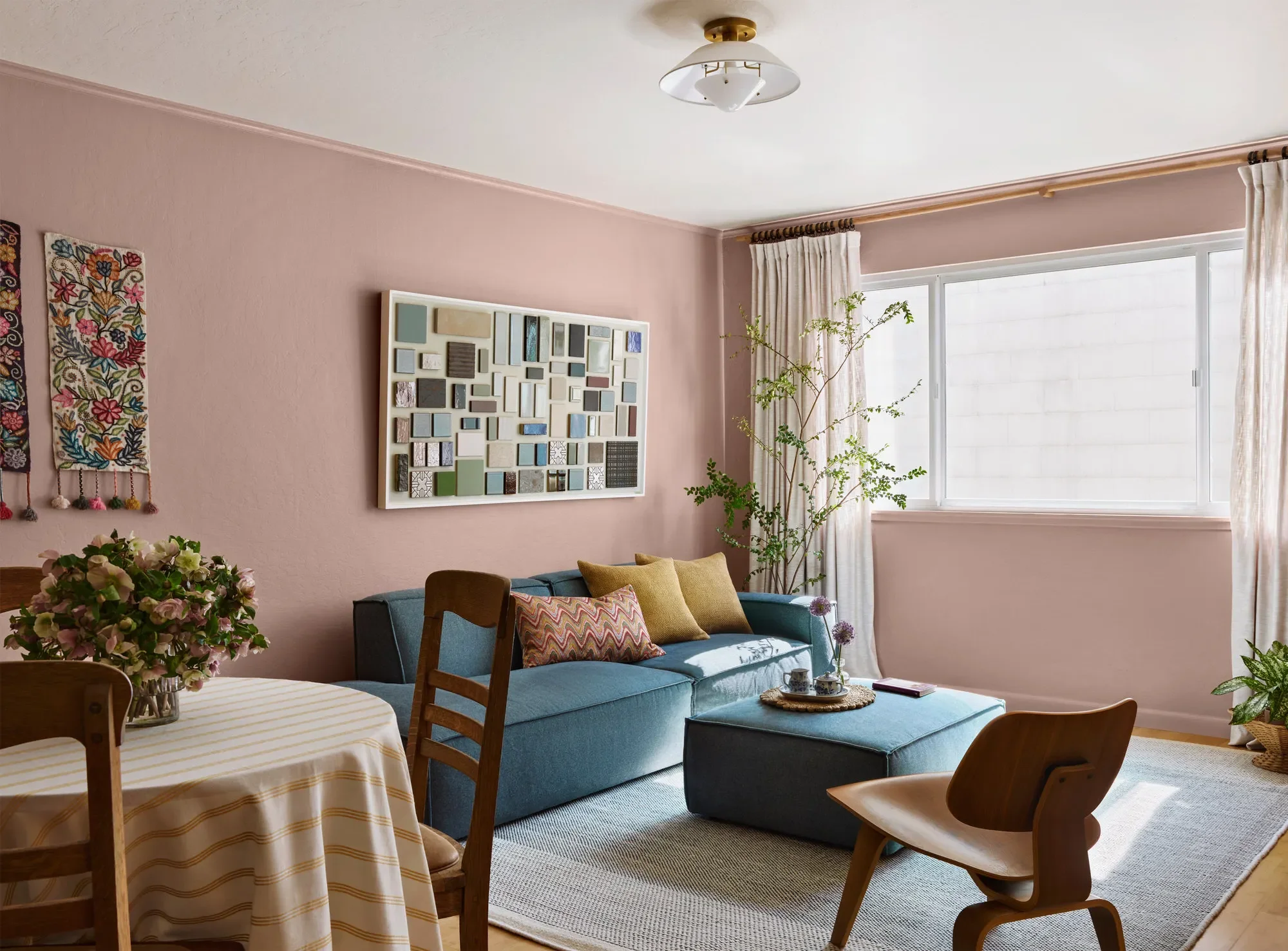 Outer Sunset living room — blush pink walls, blue sofa with mustard accents, and curated mixed-textile and tile art by Studio VAE. (