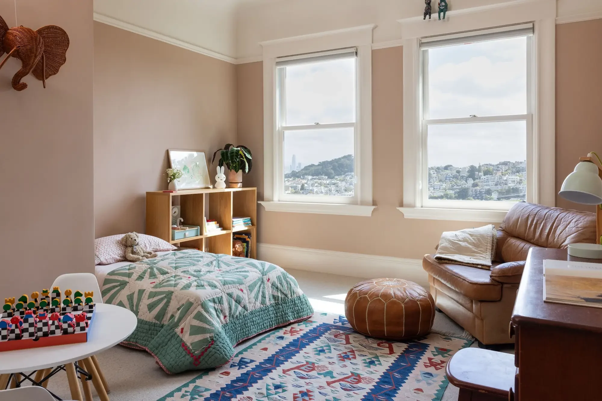 Kids bedroom with blush pink walls, patterned quilt, and San Francisoc city view in a Parnassus Heights home by Studio VAE