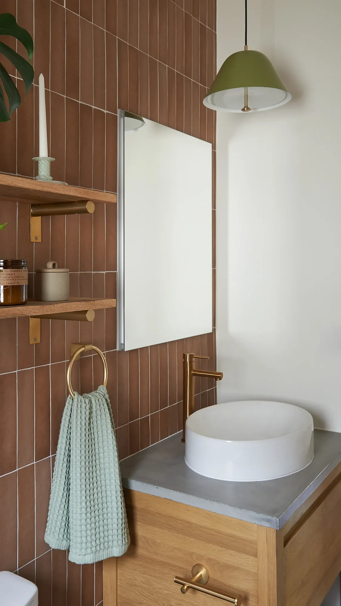 Bathroom with vertical terracotta tile, oak vanity with concrete counter and white vessel sink, and green pendant light in Lower Dimond Oakland home designed by Studio VAE, Bay Area interior designer.
