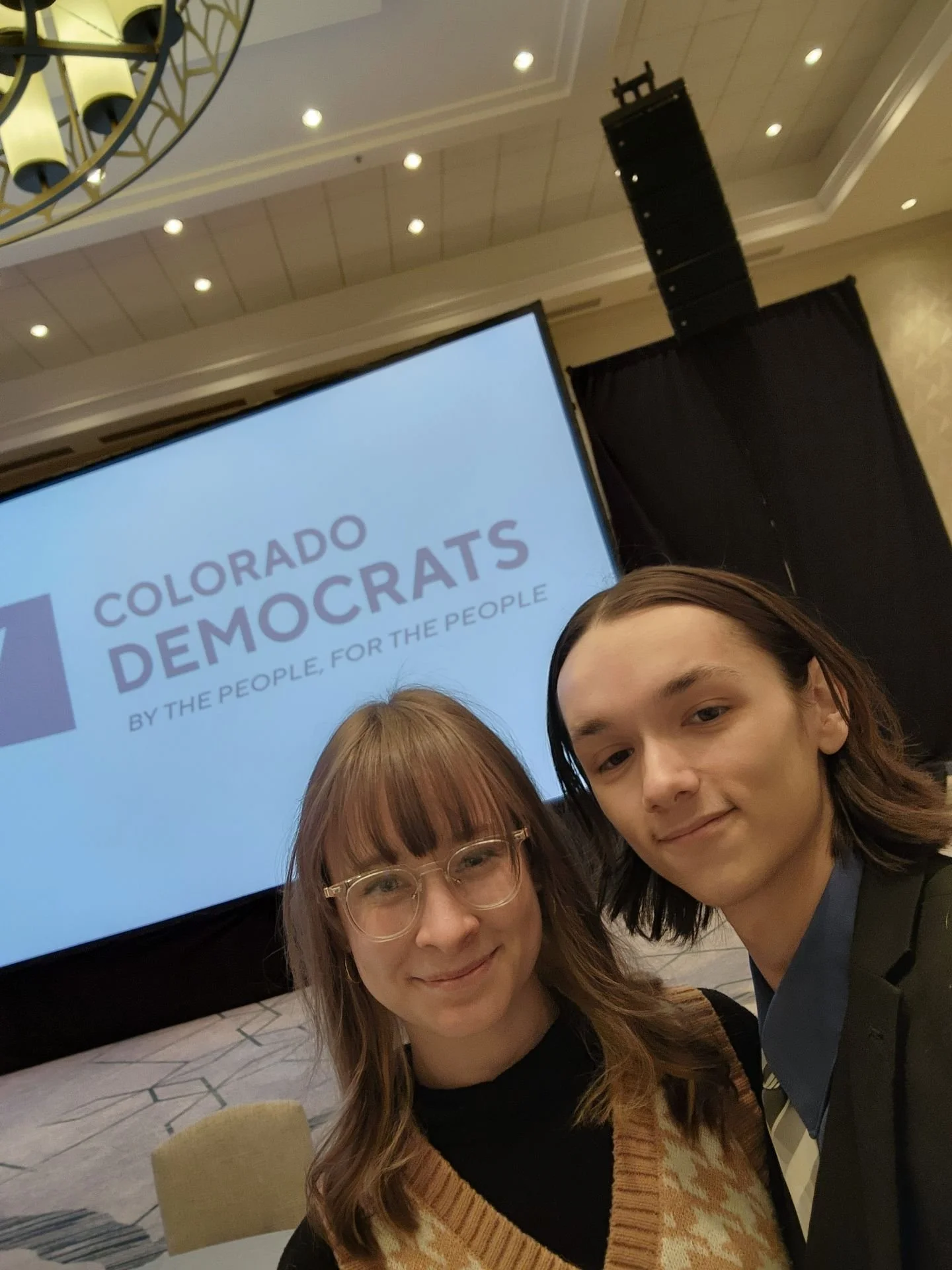 Two people posing in front of "Colorado Democrats" presentation screen at an event.