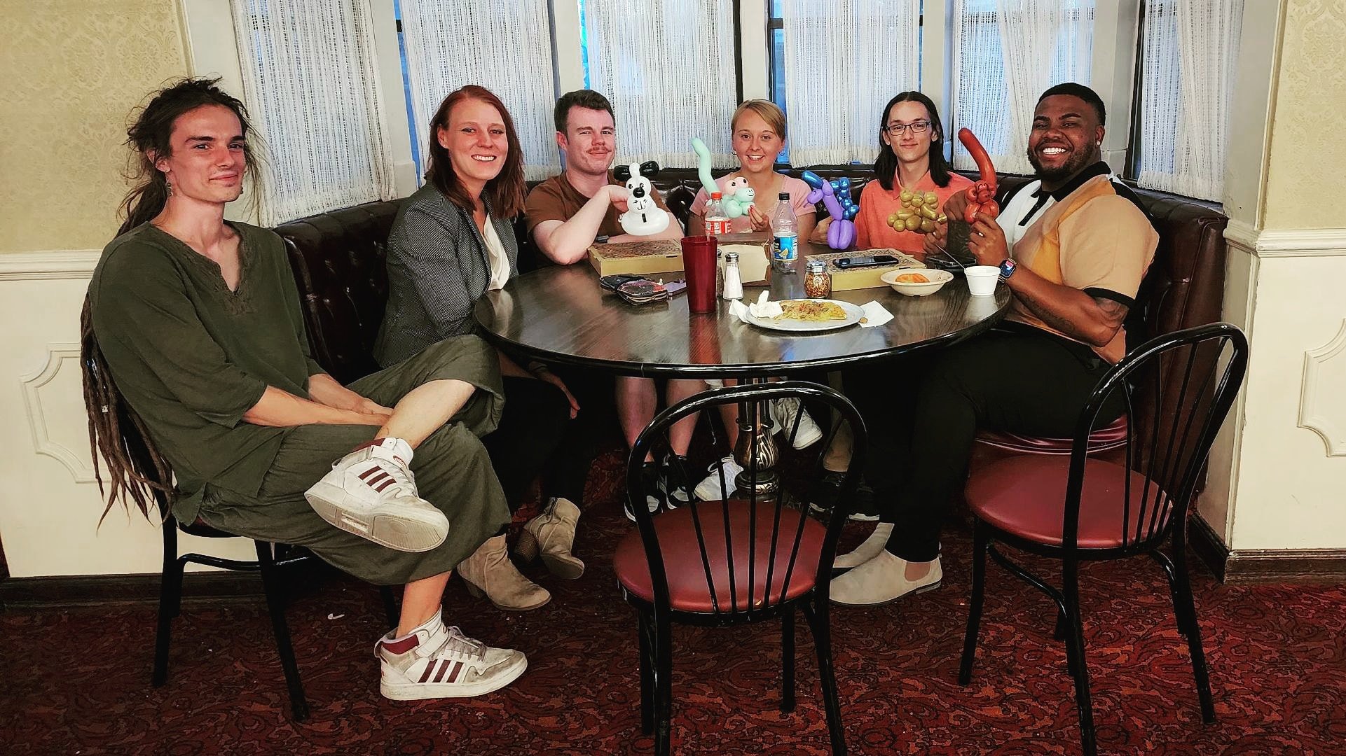 Group of six people sitting at a restaurant table with balloon animals.